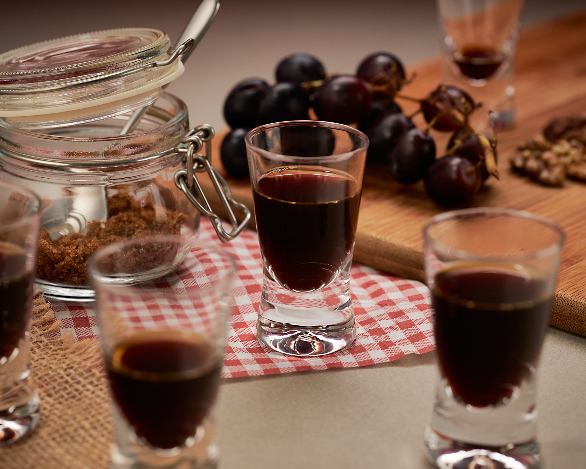 Lifestyle image of shot glasses, containing coffee, next to a chopping board with grapes and walnuts, and a pot with raw sugar, for a rustic vibe. Image by Stefania Calderara