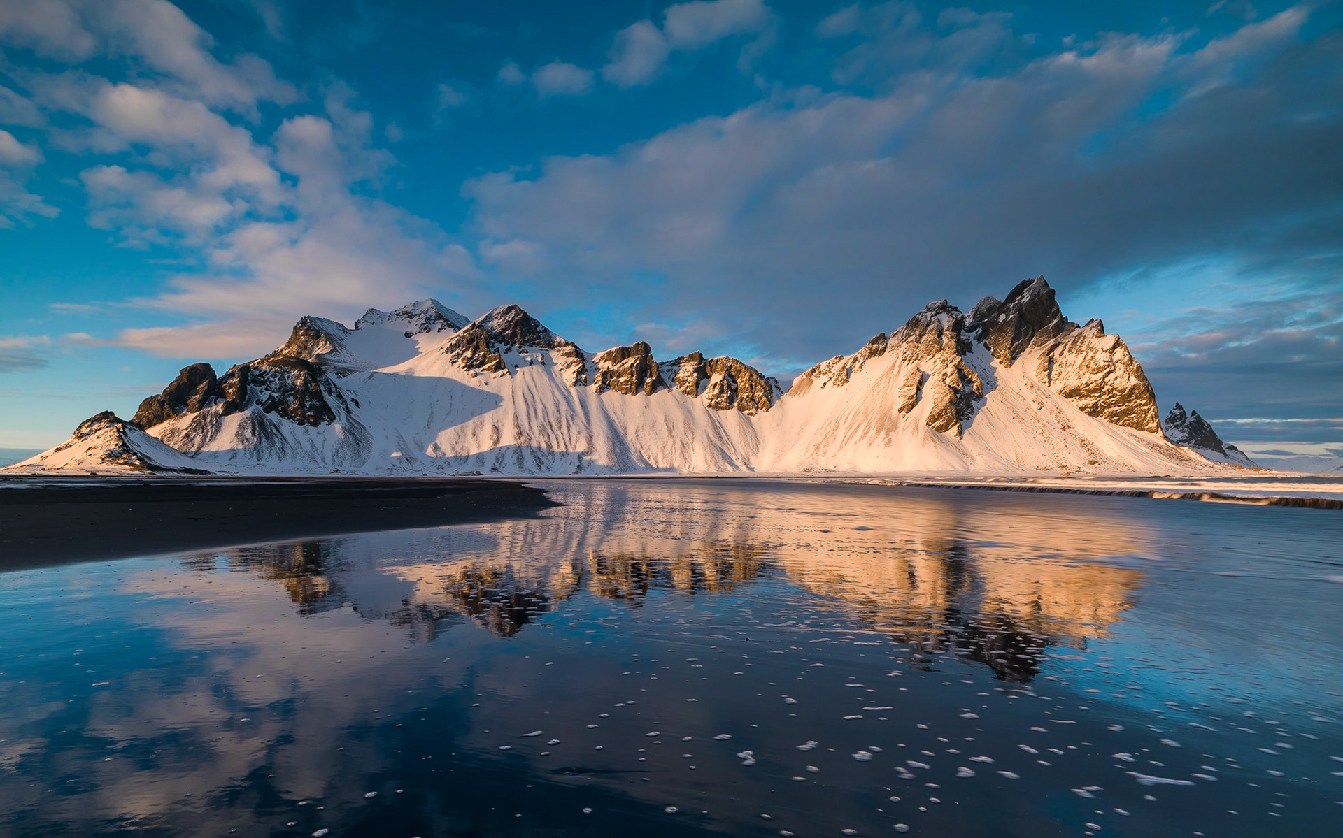 From the viewpoint of Stokksnes westrahorn is reflecting itself in the Atlantic Ocean flowing onto the beach of black sand.