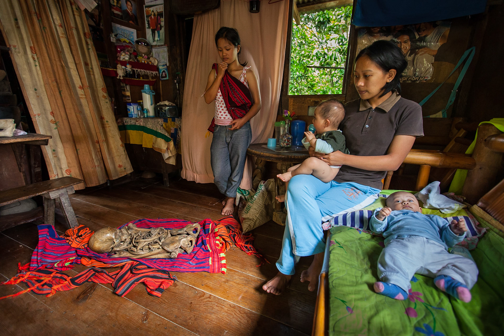 Young Ifugao girl displays her great grandfather, while her sister with kids respectfully watches. Ifugao people pray to their ancestors whom they keep in the house.