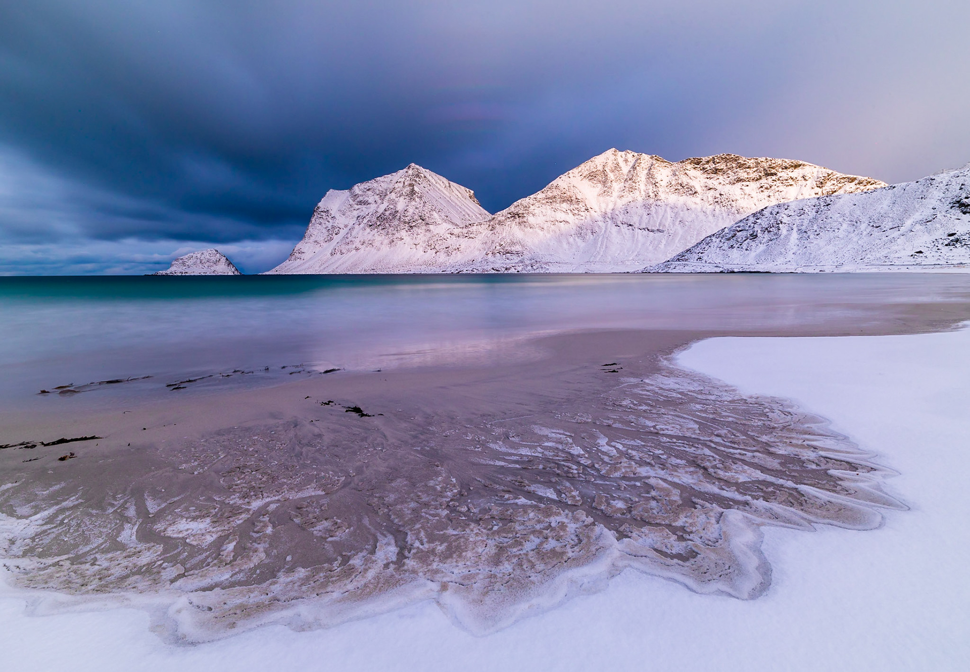 The famous Haukland Beach in Lofoten. When I arrirved the sun was coming up and shining nicely on the beach and Mountains, while at the same time snow showers were showing in the horizon.