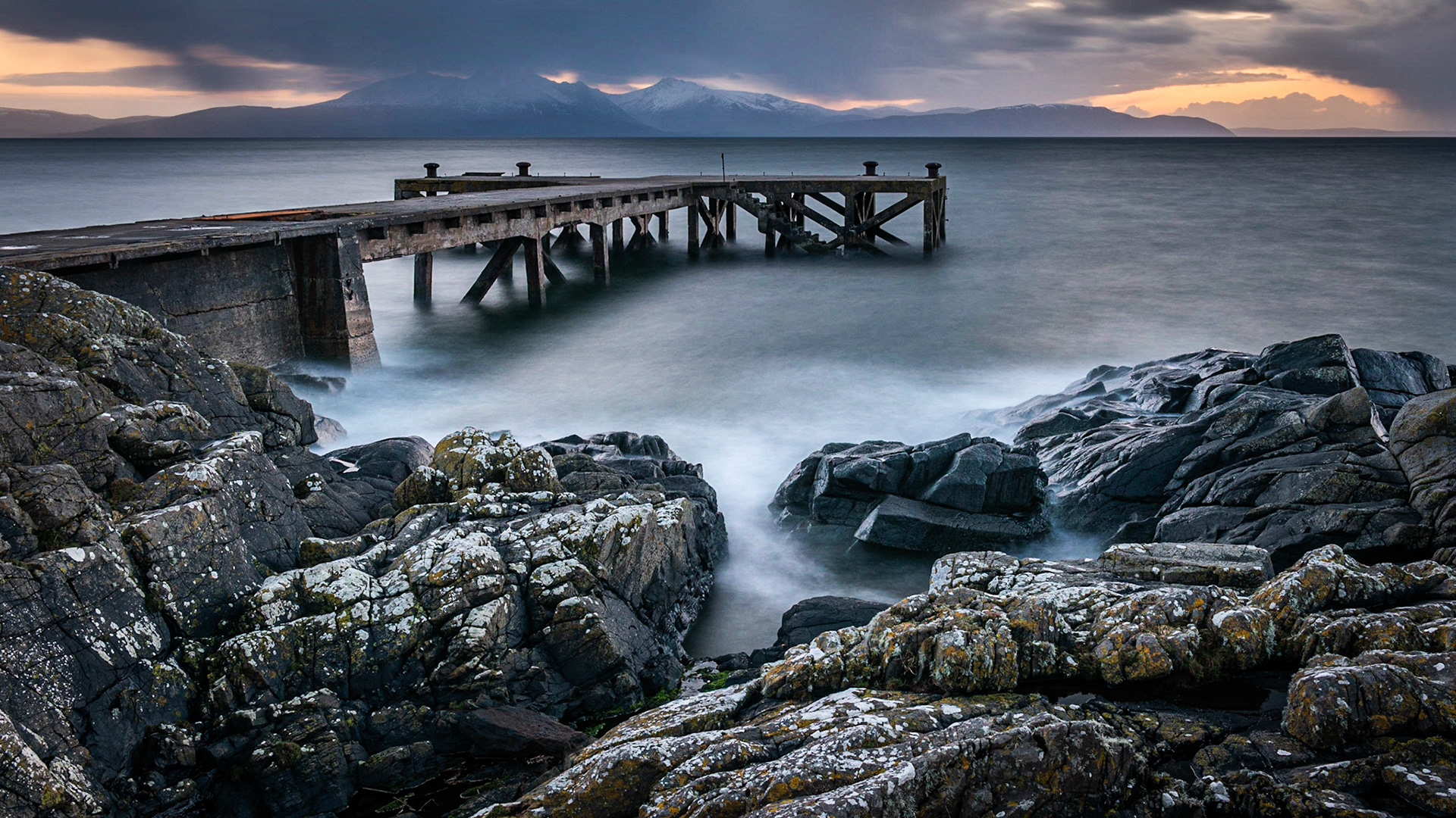 The old jetty at Portencross in Scotland and winter hills on the isle of Arran just as the sun goes down producing a dramatic sunset sky.