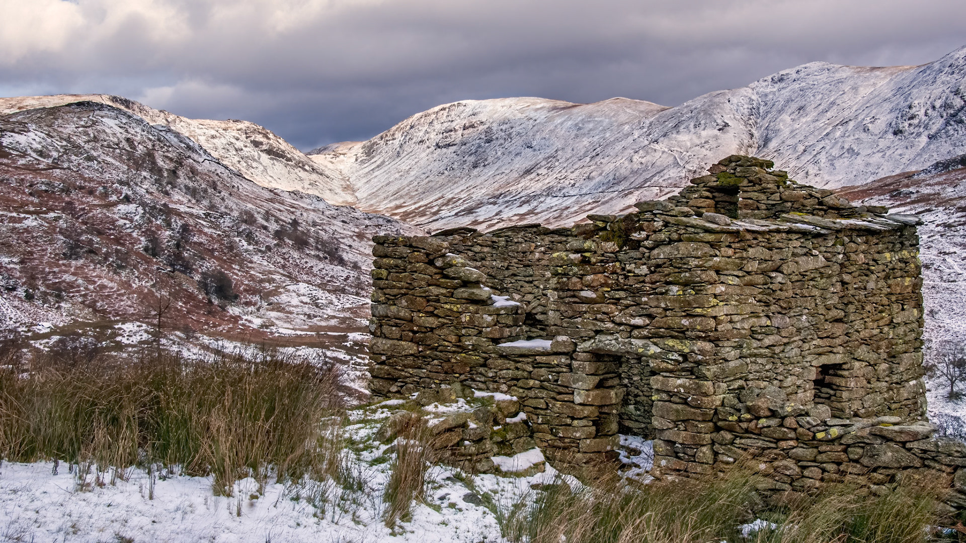The remains of an old stone barn in the Lake District near the summit of Kirkstone Pass with the snow covered slopes of Thornthwaite Crag in the distance