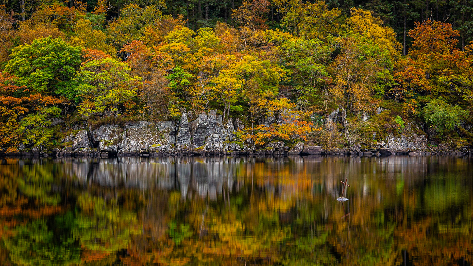 A small iron cross in the Trossachs National park reflecting in the calm autumnal waters of Loch Ard