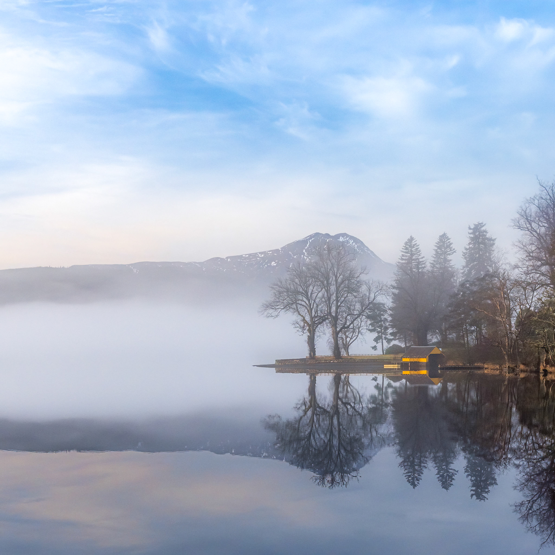 Yellow boathouse on Loch Ard in the early morning mists with Ben Lomond in background
