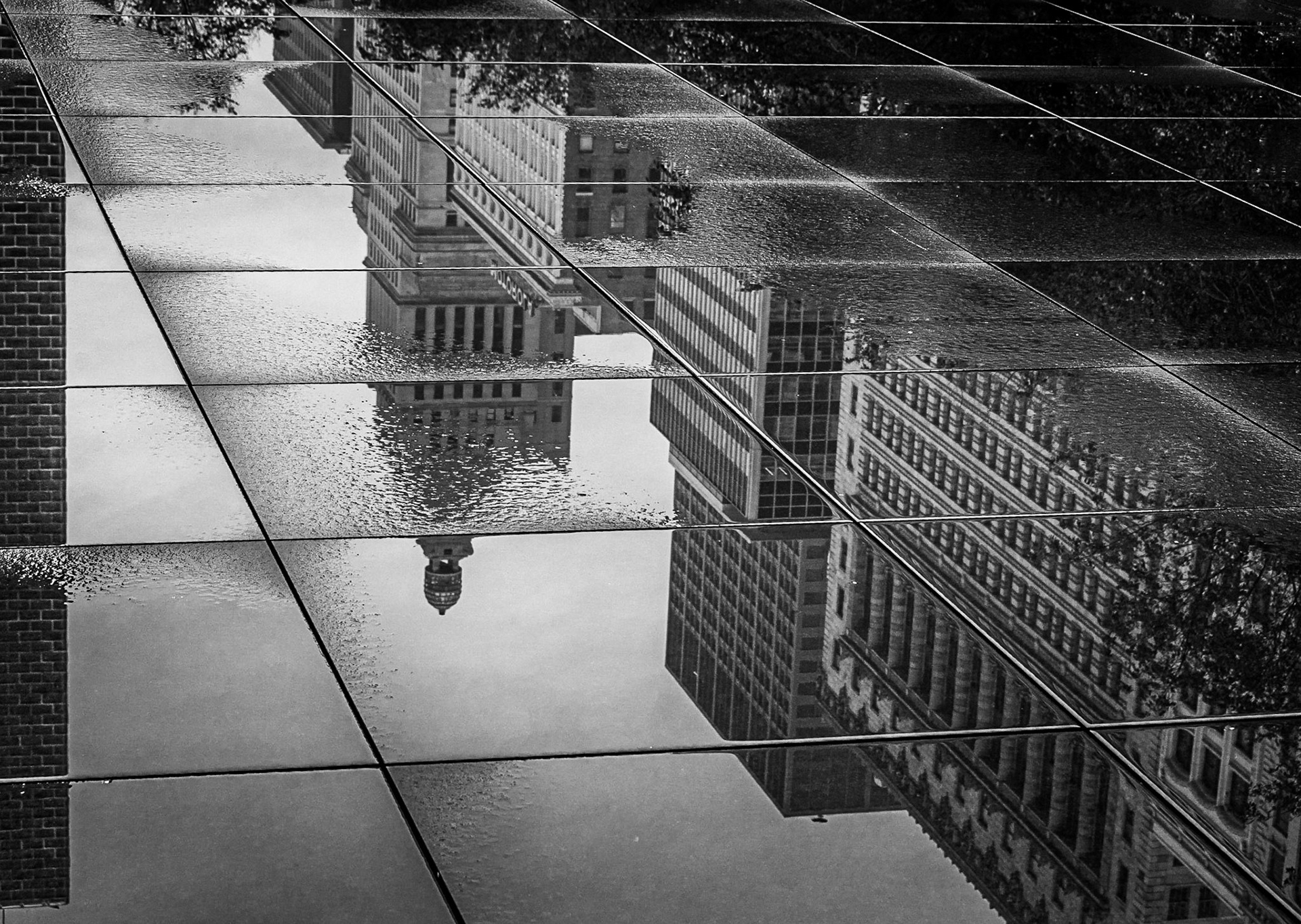 Reflections of nearby buildings are captured in the puddles on the pathway in downtown Chicago