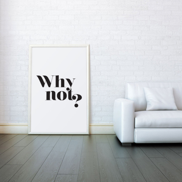 Framed "Why not?" motivational poster leaning against textured white wall on dark wooden floor in a modern minimalist living room with white sofa.