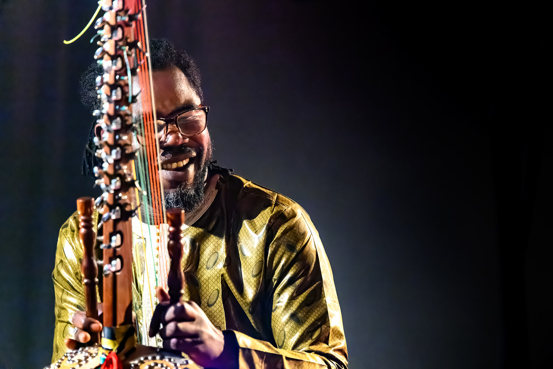 Joueur de kora en boubou doré souriant sur scène, concert de musique ouest-africaine 