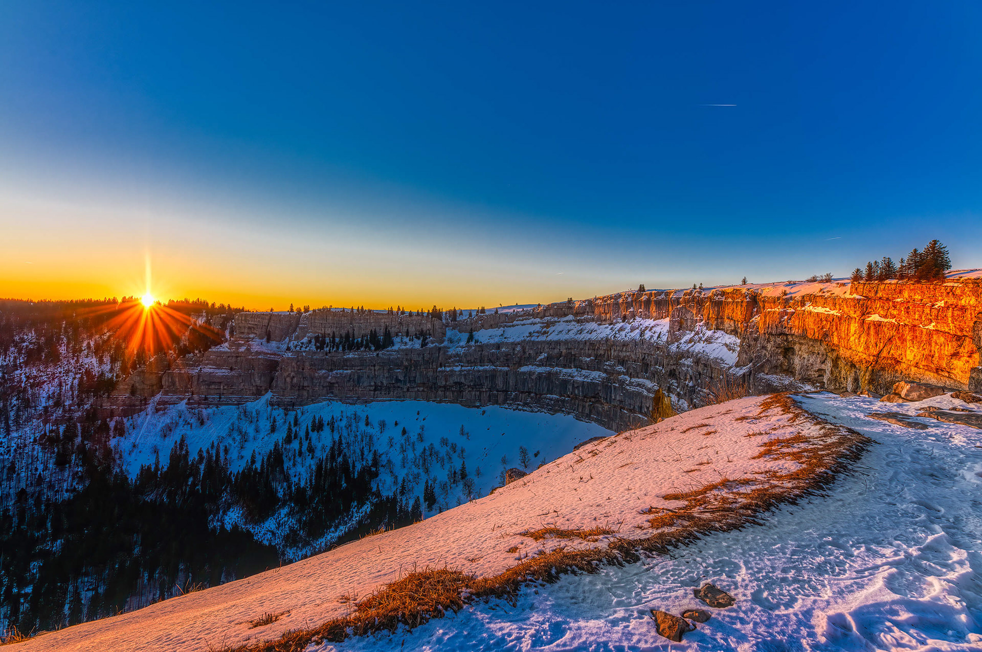 Lever de soleil hivernal sur les falaises enneigées du Creux du Van, Jura suisse
