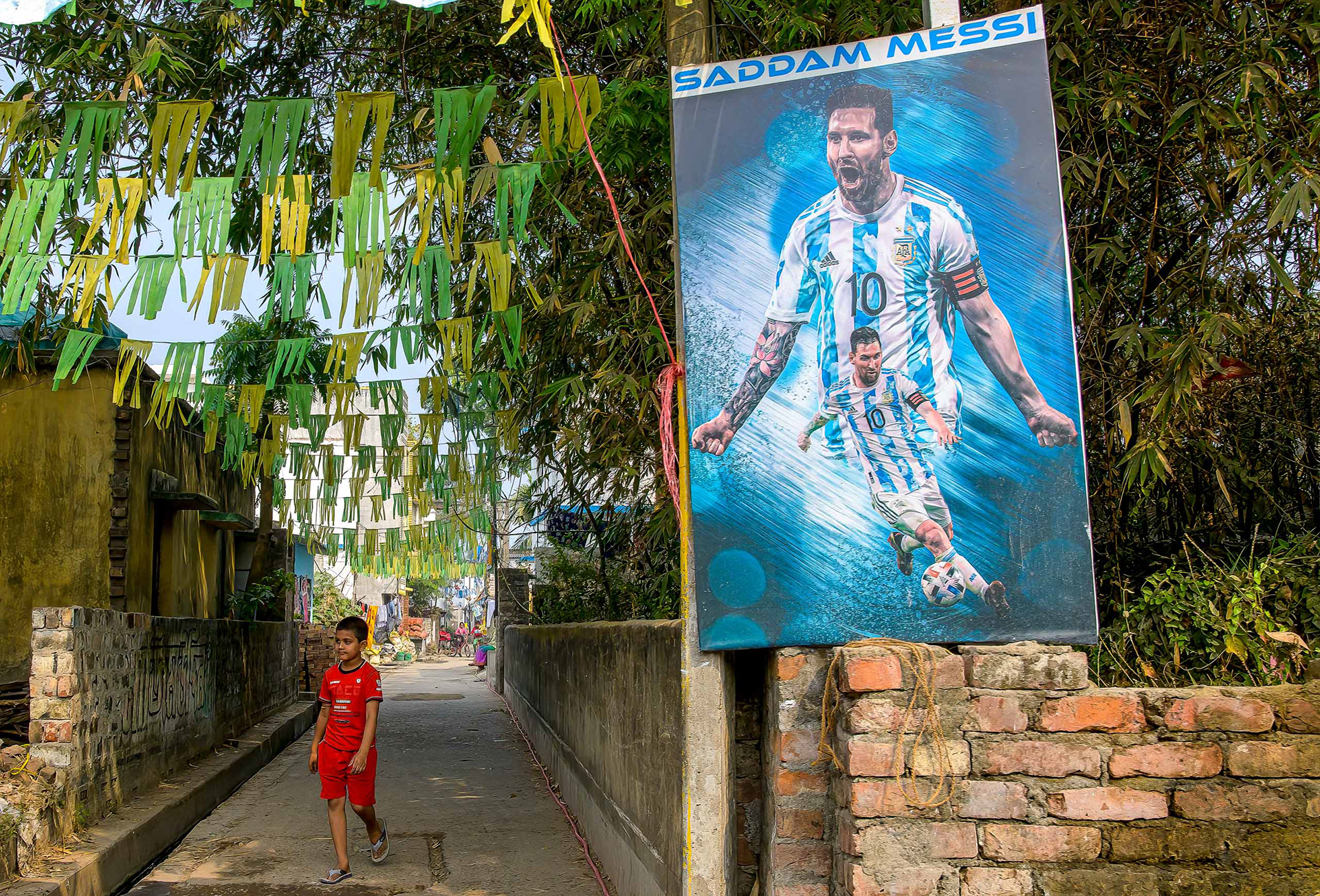 Enfant en maillot rouge sous un poster géant de Messi dans une ruelle de Kolkata en Inde — reportage