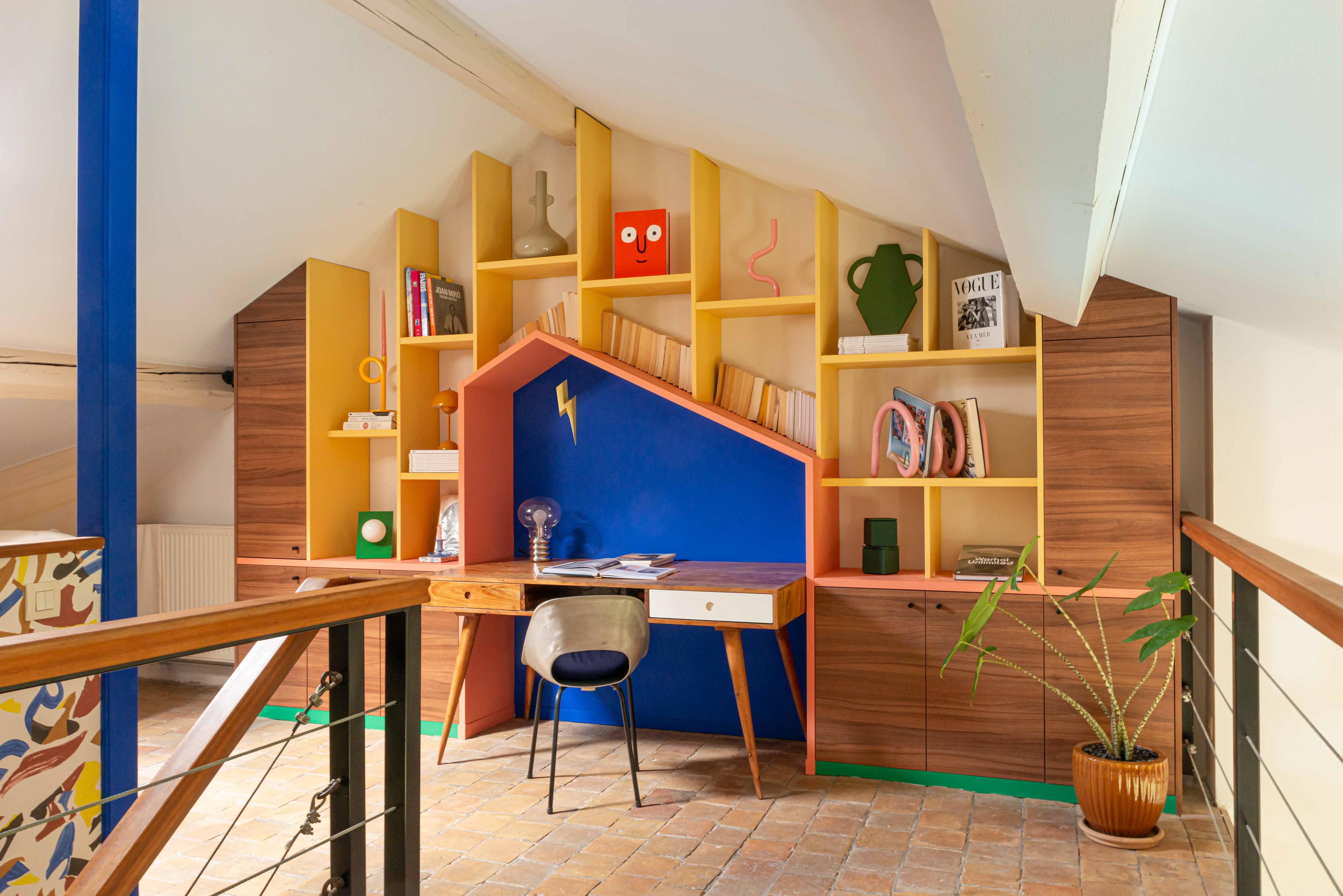 La bibliothèque aux portes décor noyer et aux lignes multicolores, est soulignée par une plinthe Vert Leaf (Plum) qui lui confère un sacré caractère ! Conçu comme un toit abritant le bureau, l’endroit est idéal pour travailler, créer, dessiner, rêver… et voir en grand !