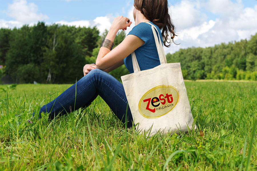 Logo seen on a tote bag over the shoulder of a woman in a field