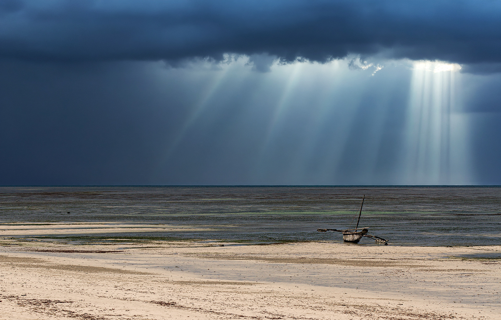 “Traditional wooden fishing boat on a quiet beach in Kenya under dramatic storm clouds, with powerful sun rays breaking through the dark sky over the Indian Ocean.”