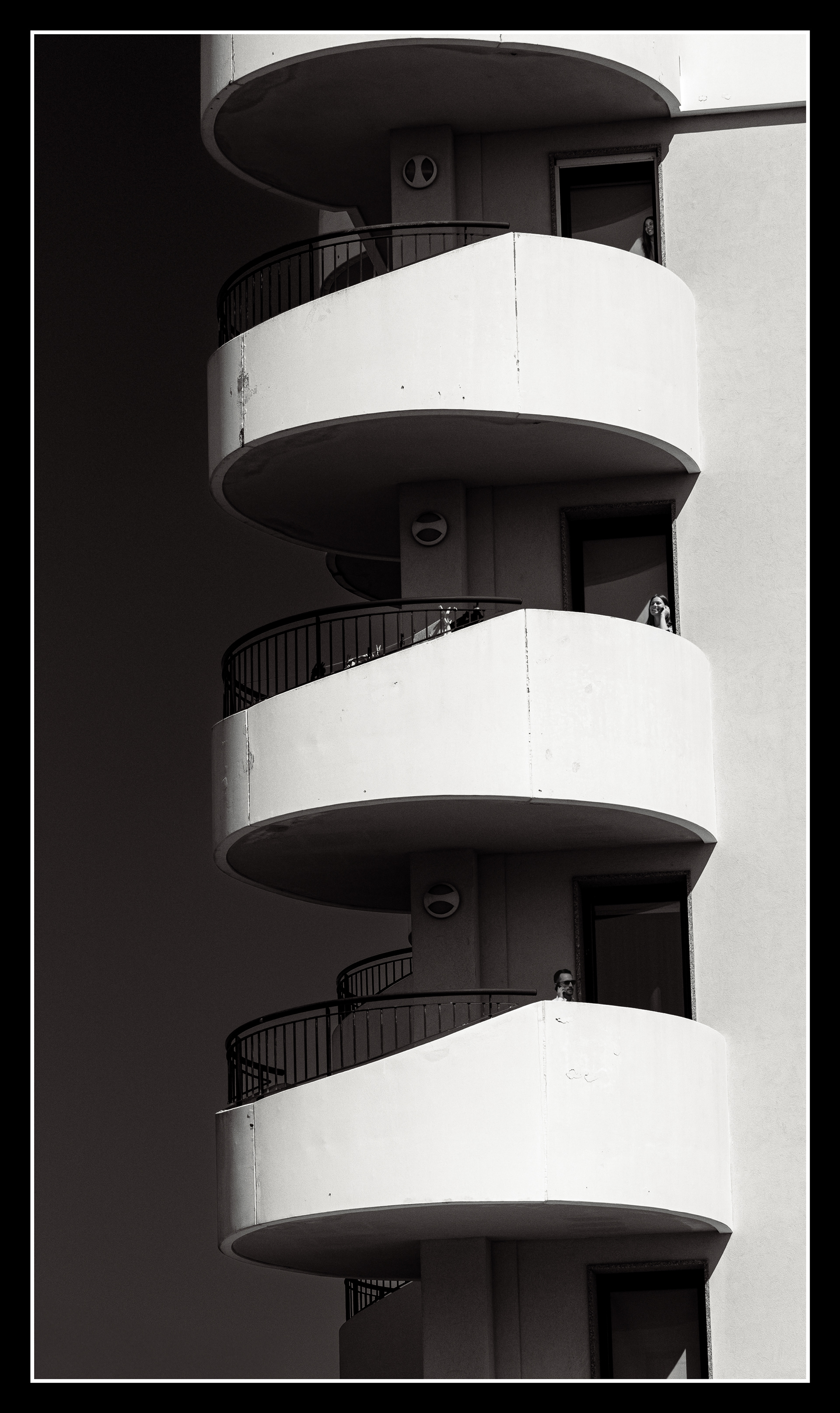 Black and white architectural photo of curved balconies with a single woman, minimal fine art style, Grado Italy, Minimalist black and white architectural photography capturing the repetition of curved balconies and a single human presence. The image plays with light, shadow and geometry, creating a calm and timeless fine art composition. Taken in Grado, Italy.