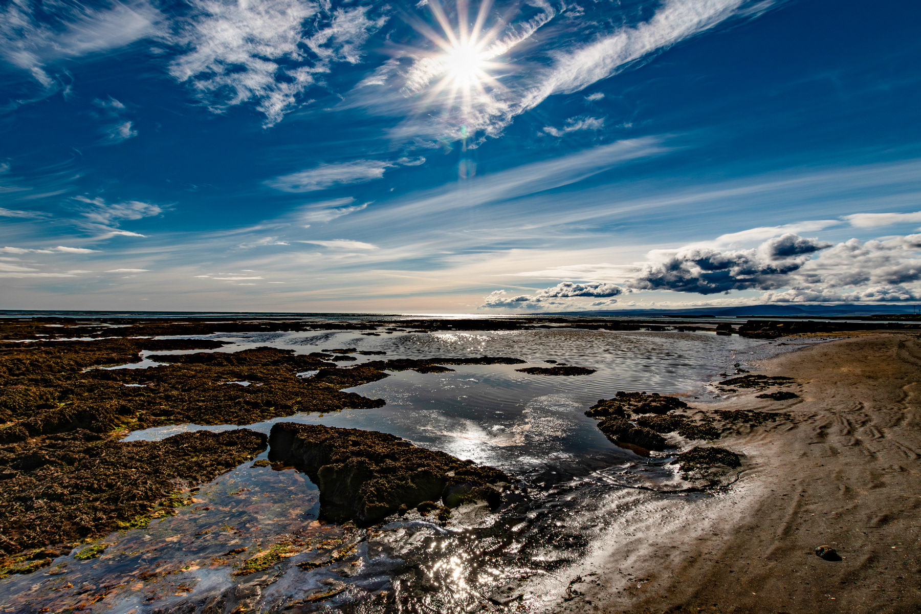Iceland coastal landscape with volcanic shoreline, tidal pools, sunburst sky and dramatic Arctic cloud formations.Sunburst over a volcanic shoreline in Iceland with tidal pools, dramatic cloud formations and reflective coastal waters.