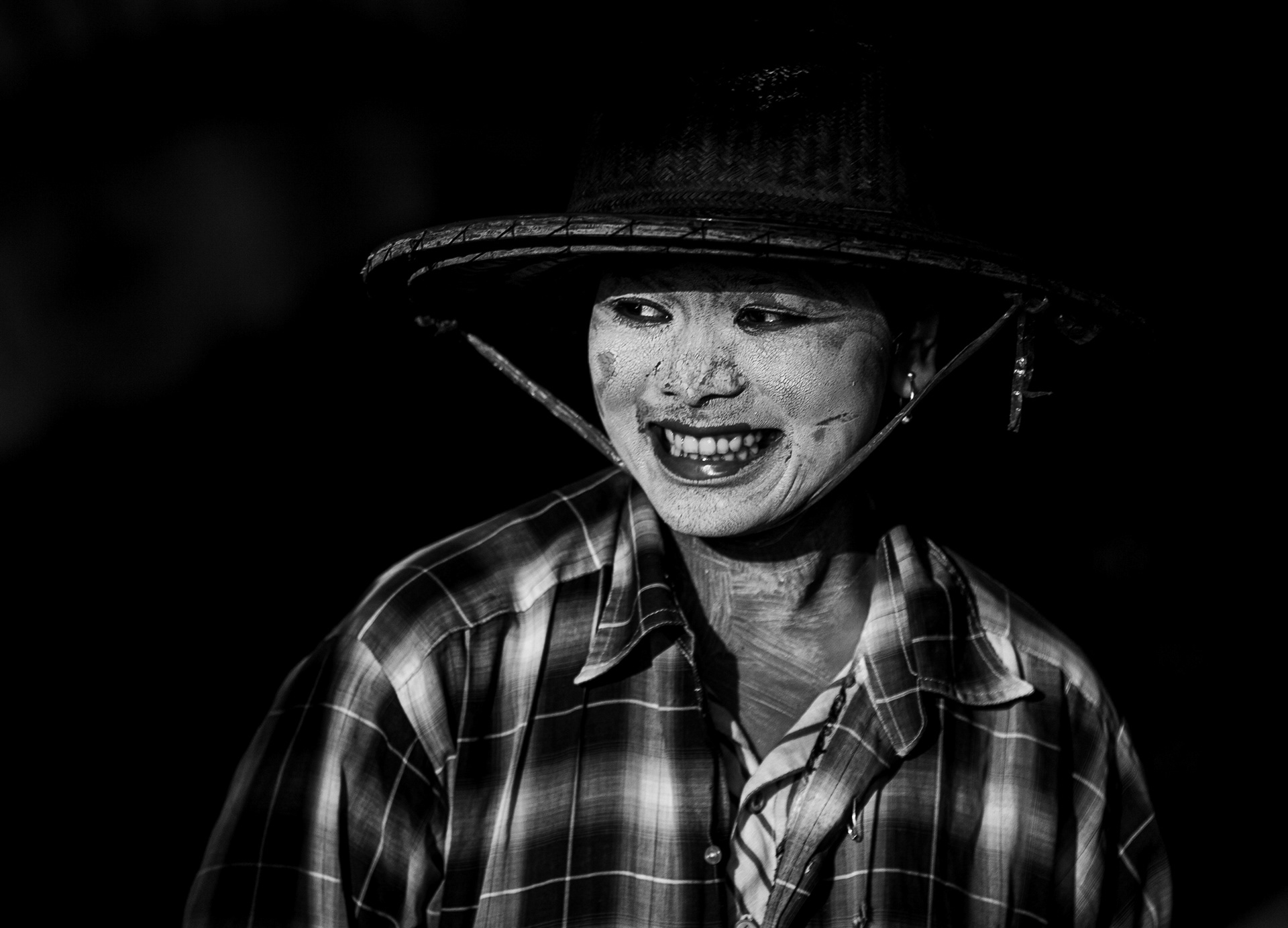 Black and white street portrait of a man sitting on the ground, looking directly at the camera, with strong contrast and emotional expression.