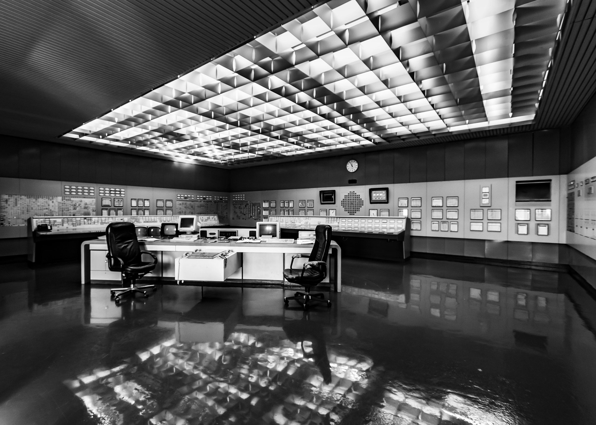 Black and white photograph of an abandoned nuclear power plant control room with chairs, control panels and reflective floor in Zwentendorf, Austria.