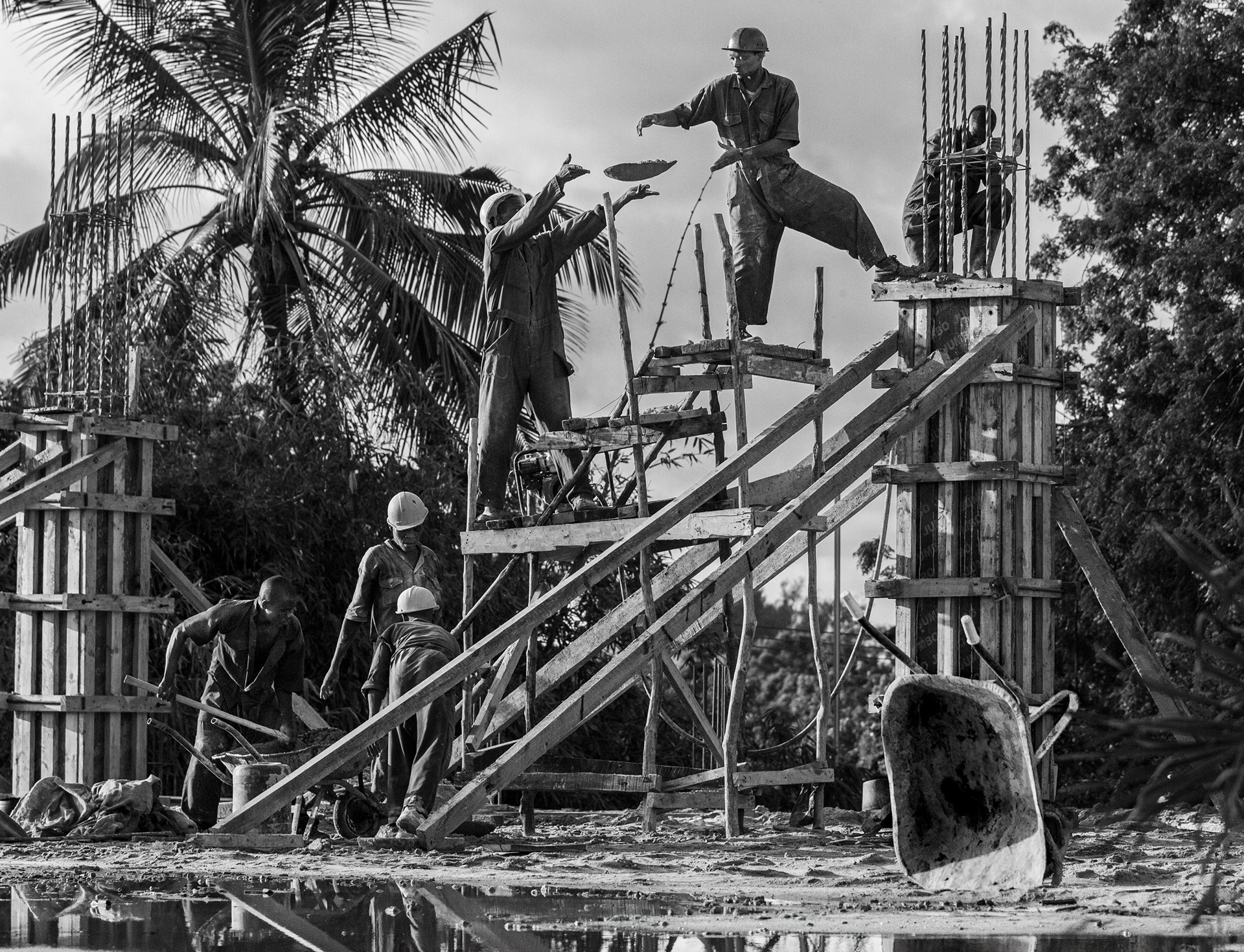 Black and white documentary photograph of Kenyan construction workers passing concrete by hand on a timber scaffold.