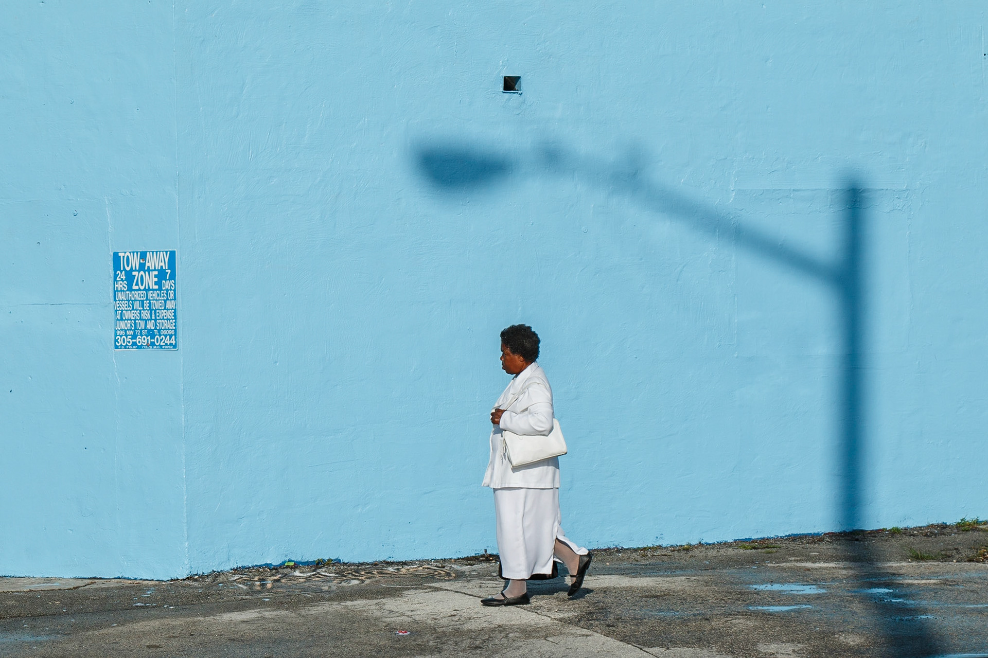 Women dressed in her Sunday best is framed by a shadow of a streetlight on a blue wall