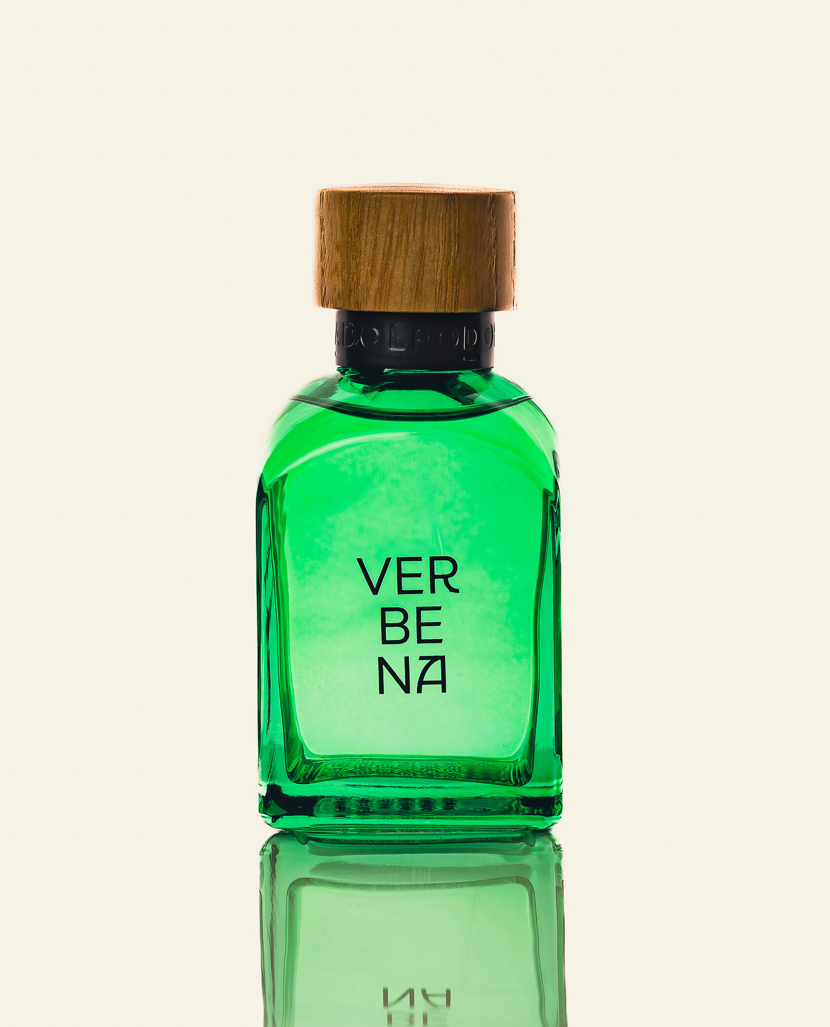 "Fotografía publicitaria de perfume Verbena en frasco de vidrio verde con tapa de madera, destacando transparencias y reflejo nítido sobre fondo claro."