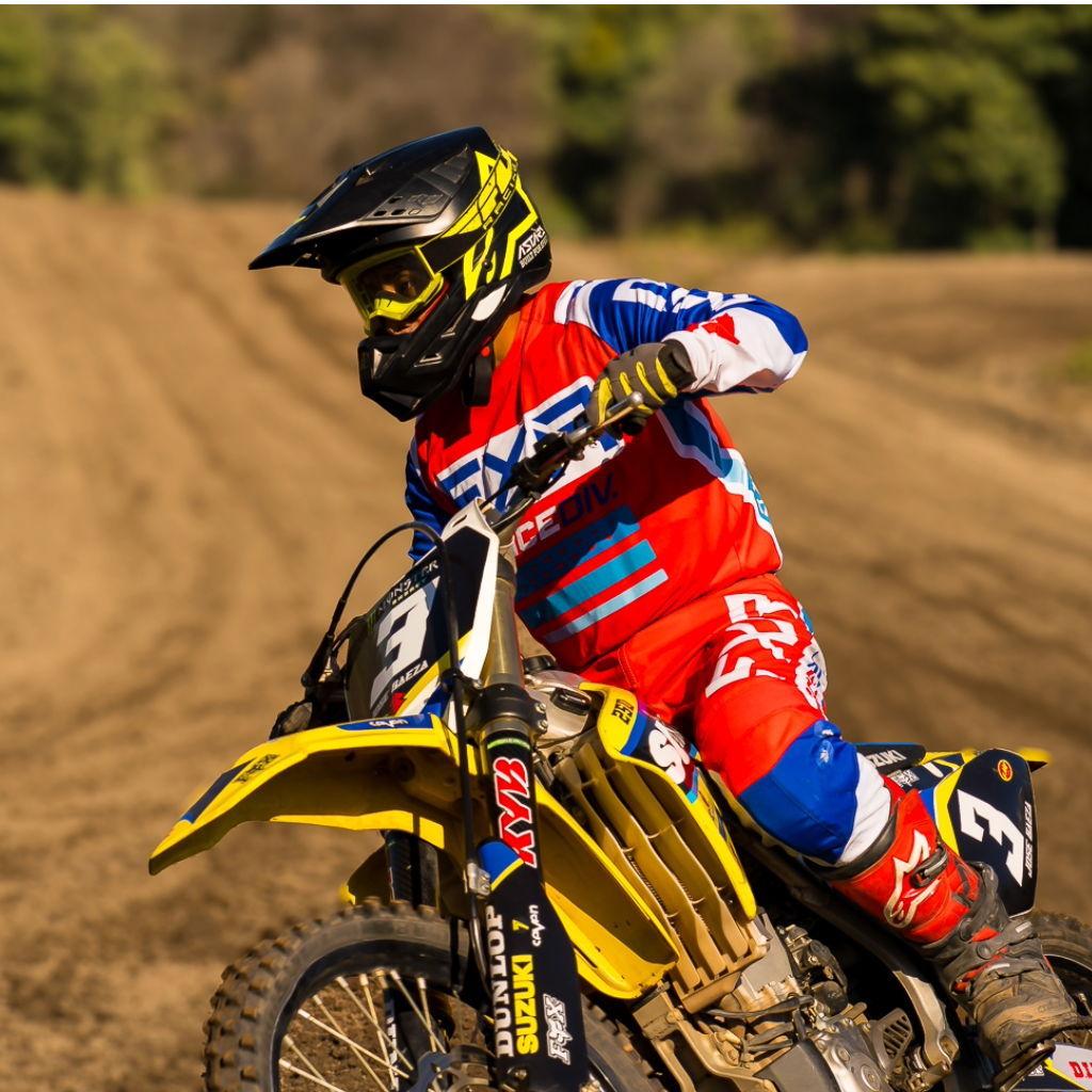 Un motorista de motocross, llevando un casco y equipo de protección, monta una motocicleta amarilla en una pista de tierra.