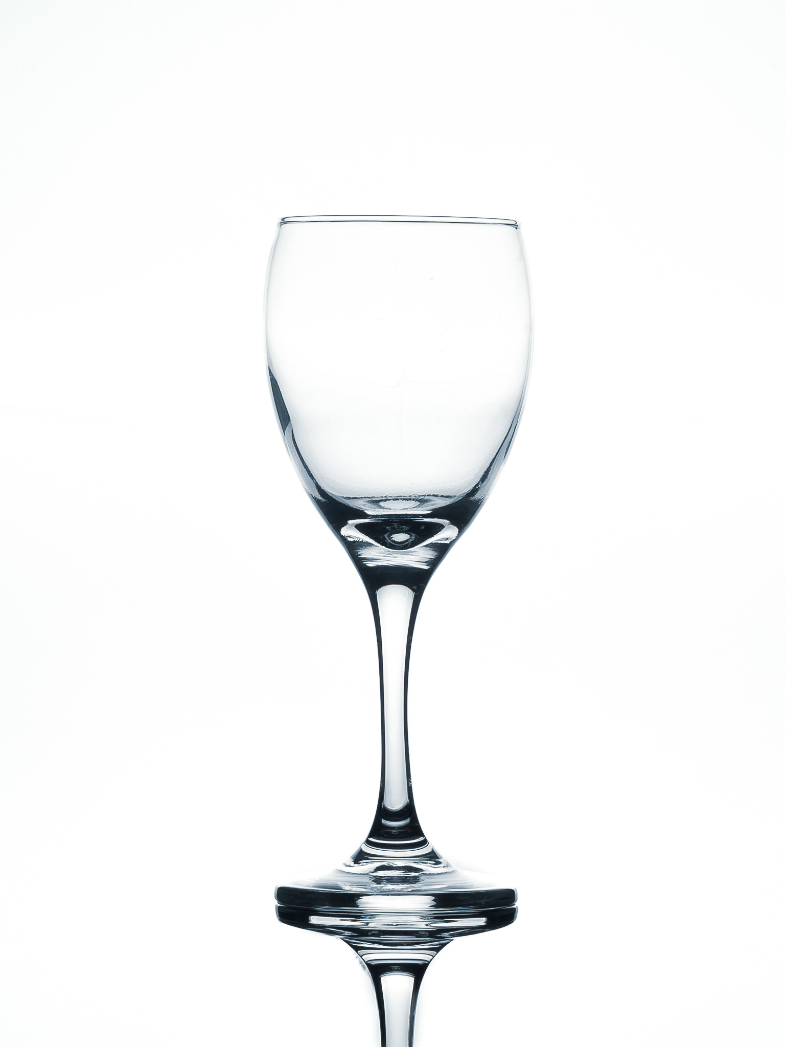 "Fotografía publicitaria de cristalería: copa de vino vacía con iluminación de borde nítida y reflejo simétrico sobre fondo blanco puro."