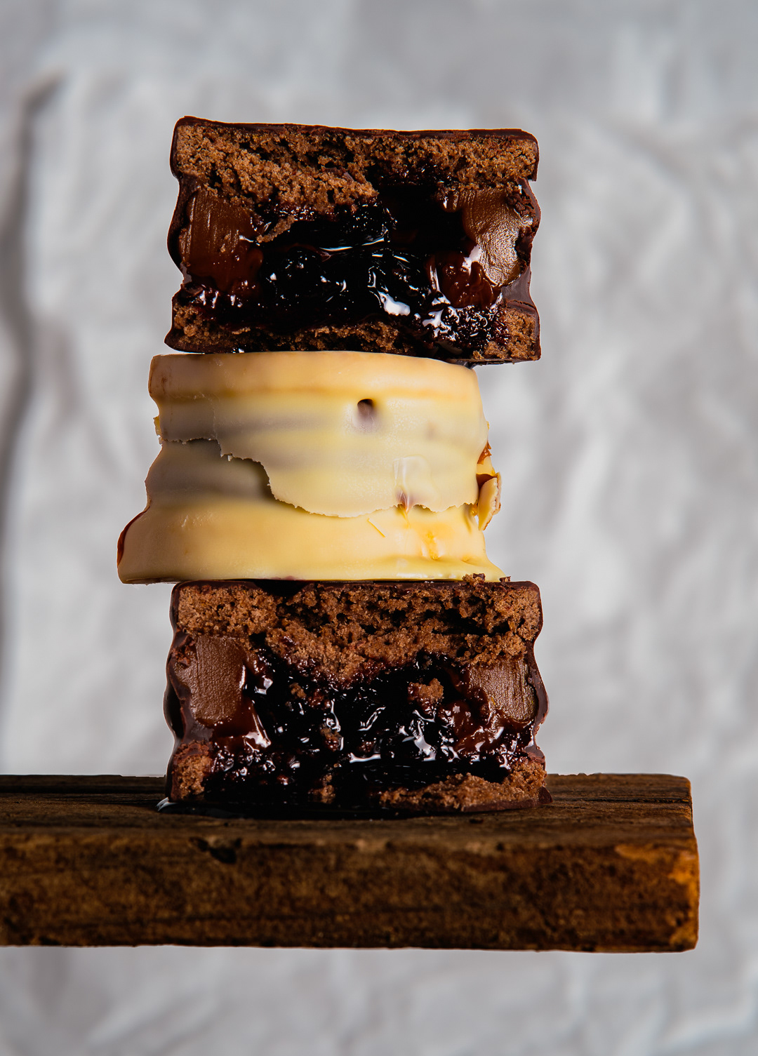 "Fotografía publicitaria de torre de alfajores artesanales con relleno de chocolate y dulce de leche, técnica de corte para resaltar texturas."