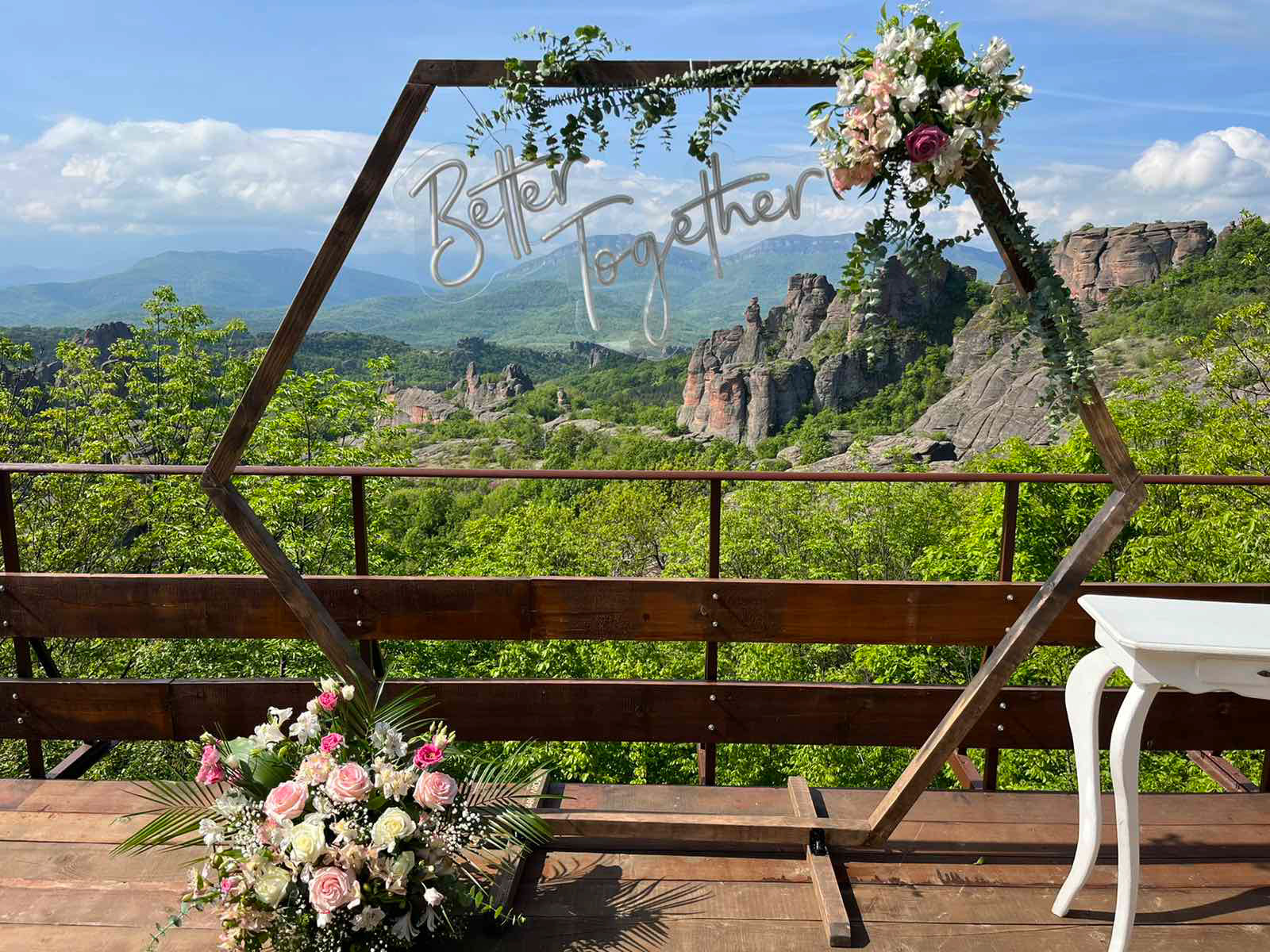 Boho hexagonal wooden wedding arch with floral decor and 'Better Together' sign, set against a scenic mountain view – perfect for modern outdoor weddings across Europe.