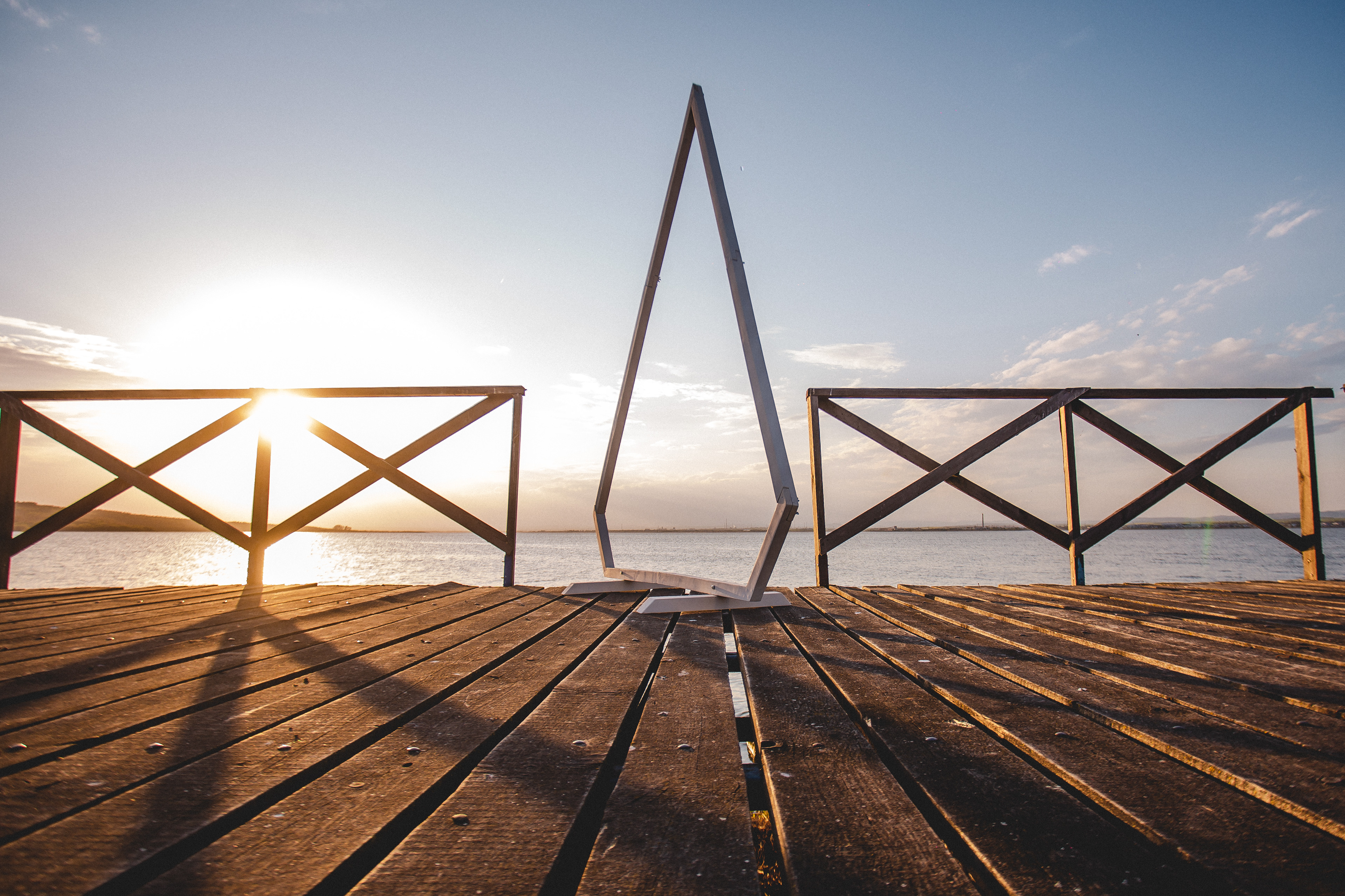 Diamond-shaped wooden wedding arch set on a beach at sunset – perfect for romantic European proposals