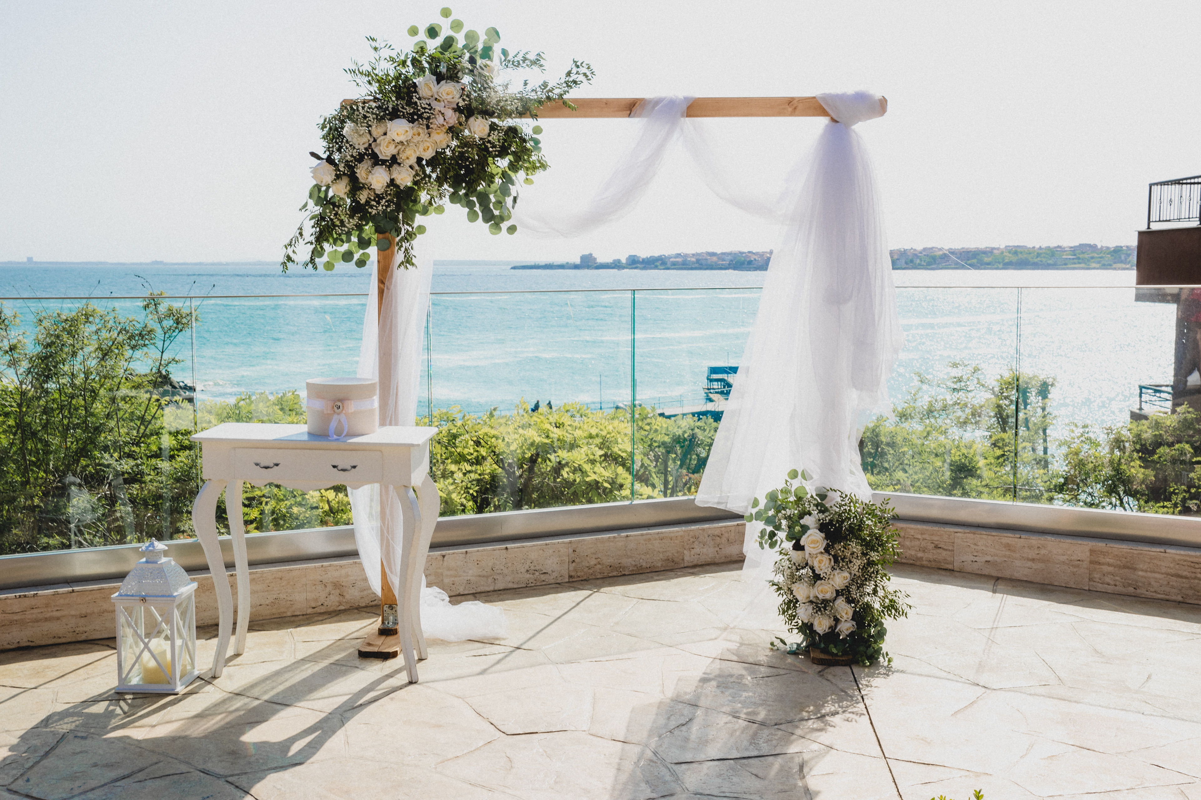 Rectangular wooden wedding arch decorated with white roses and eucalyptus, set on a seaside terrace with a view of the Black Sea – ideal for romantic ceremonies in Europe.