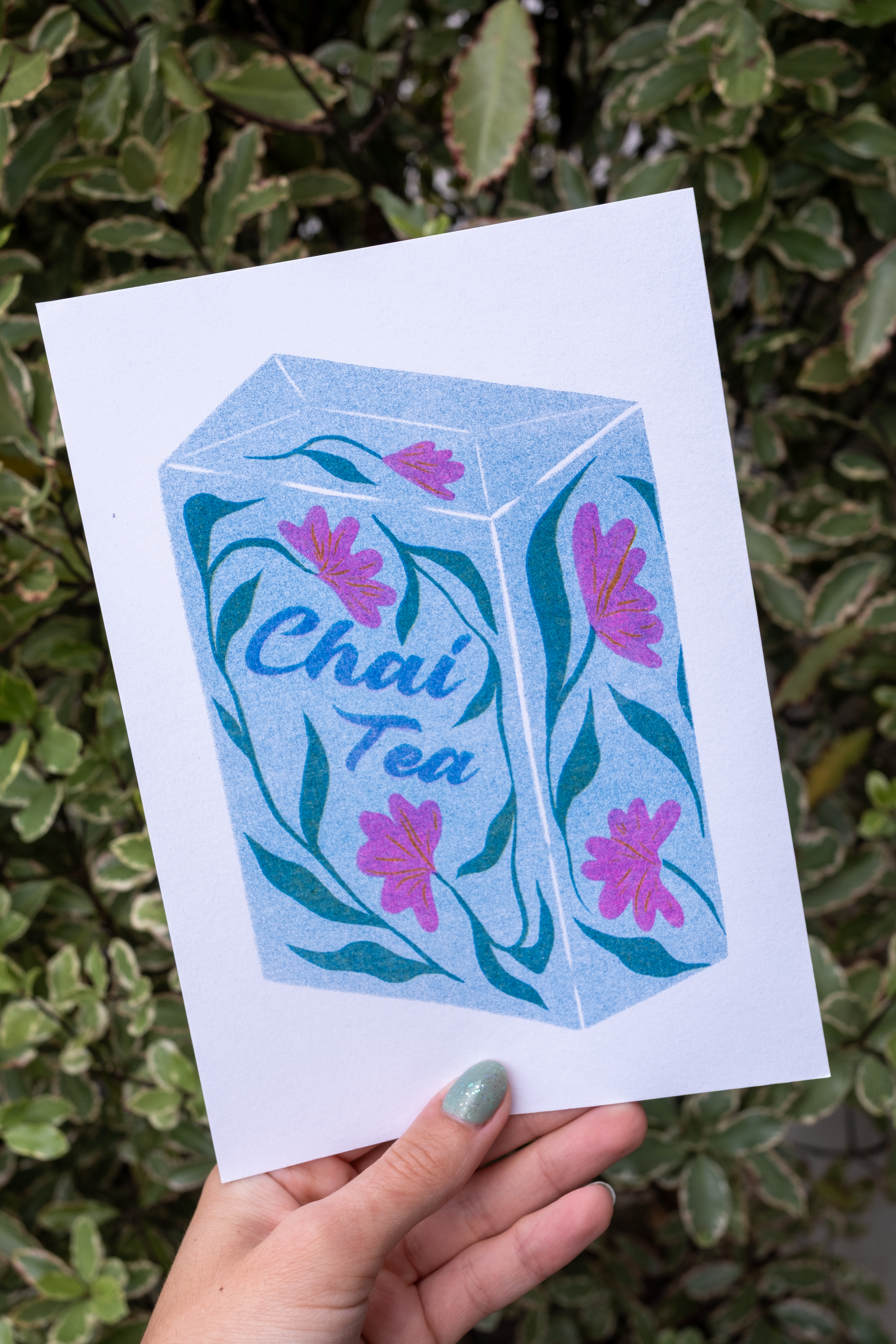 An A5 riso print of a chai tea box. Featuring floral decoration in blues, pinks and a mix of green