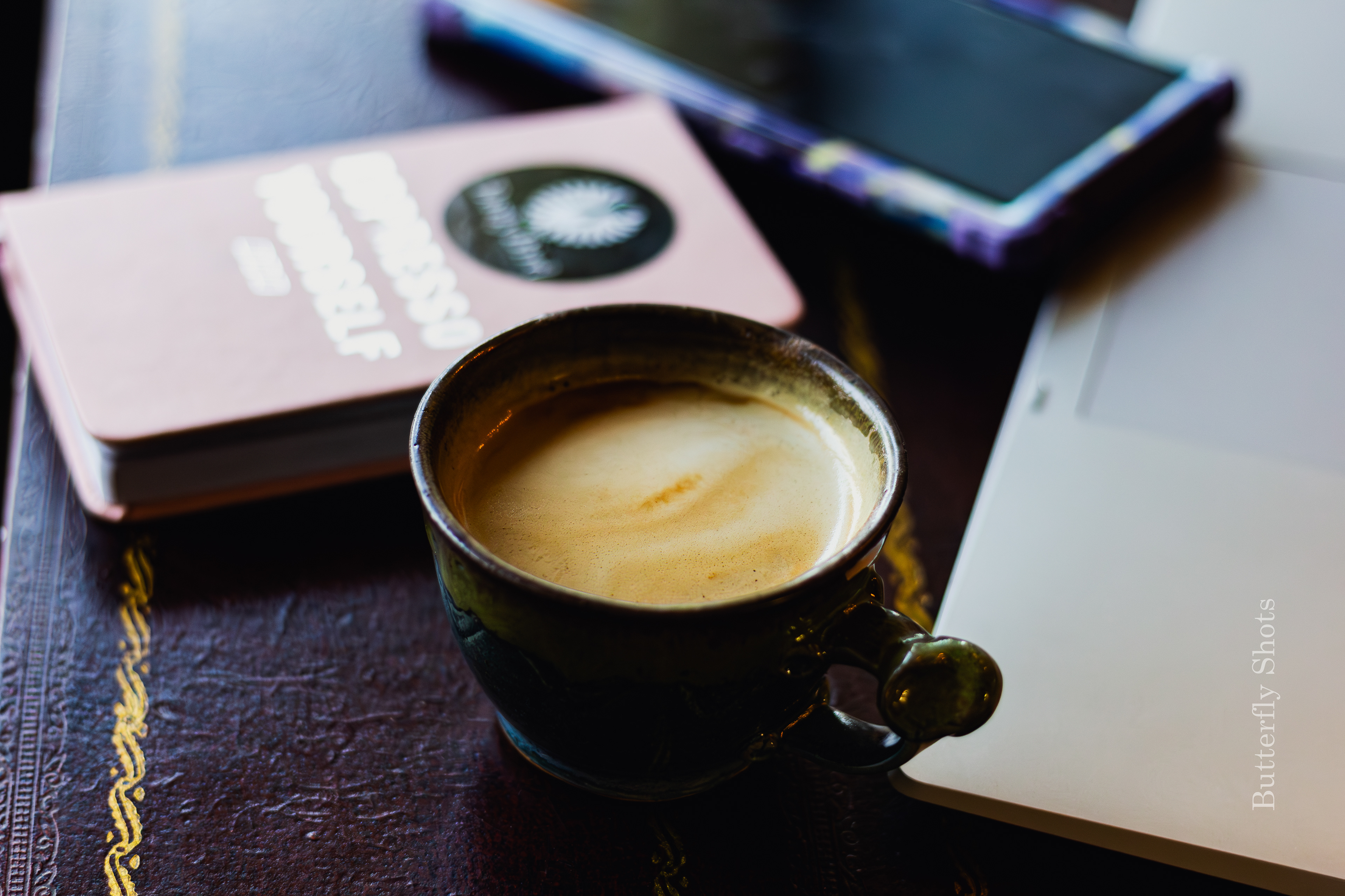 Product photography (food photography) of a cortado coffee in front of a phone and a journal