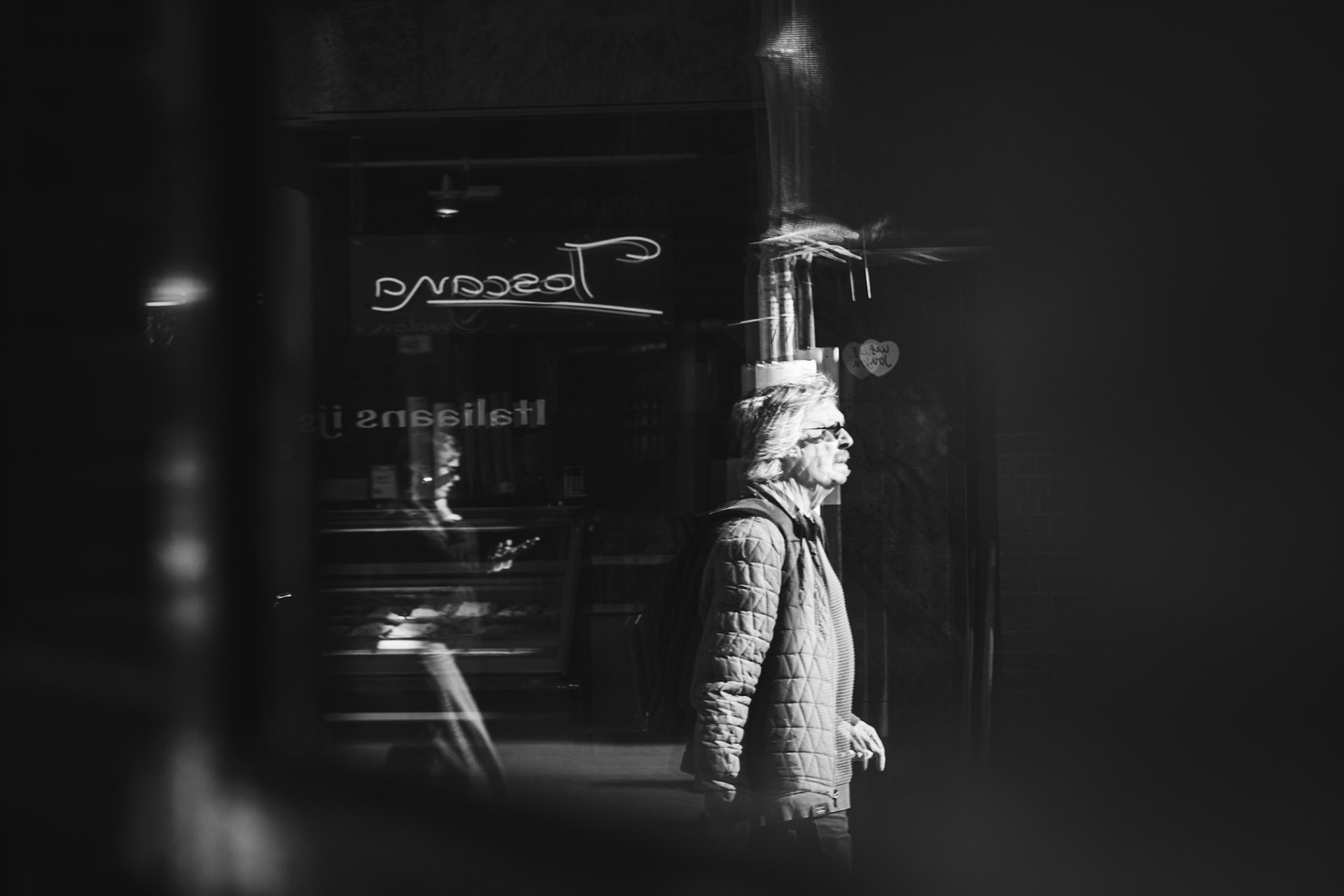 Hij passeert Toscana’s etalage in spiegelbeeld, daglicht breekt door de ramen.