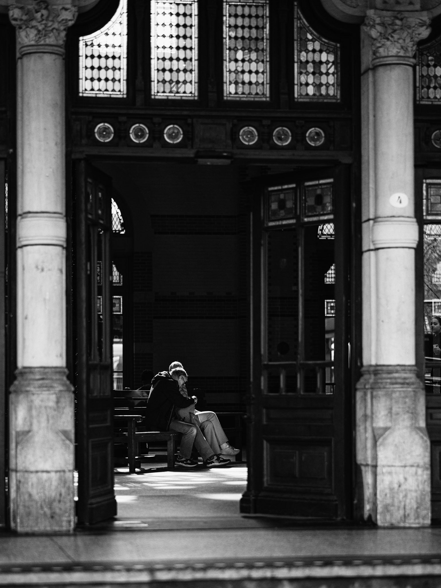 In historisch stationlicht leunt een paar naar elkaar, subframed door pilaren in tedere isolatie.
