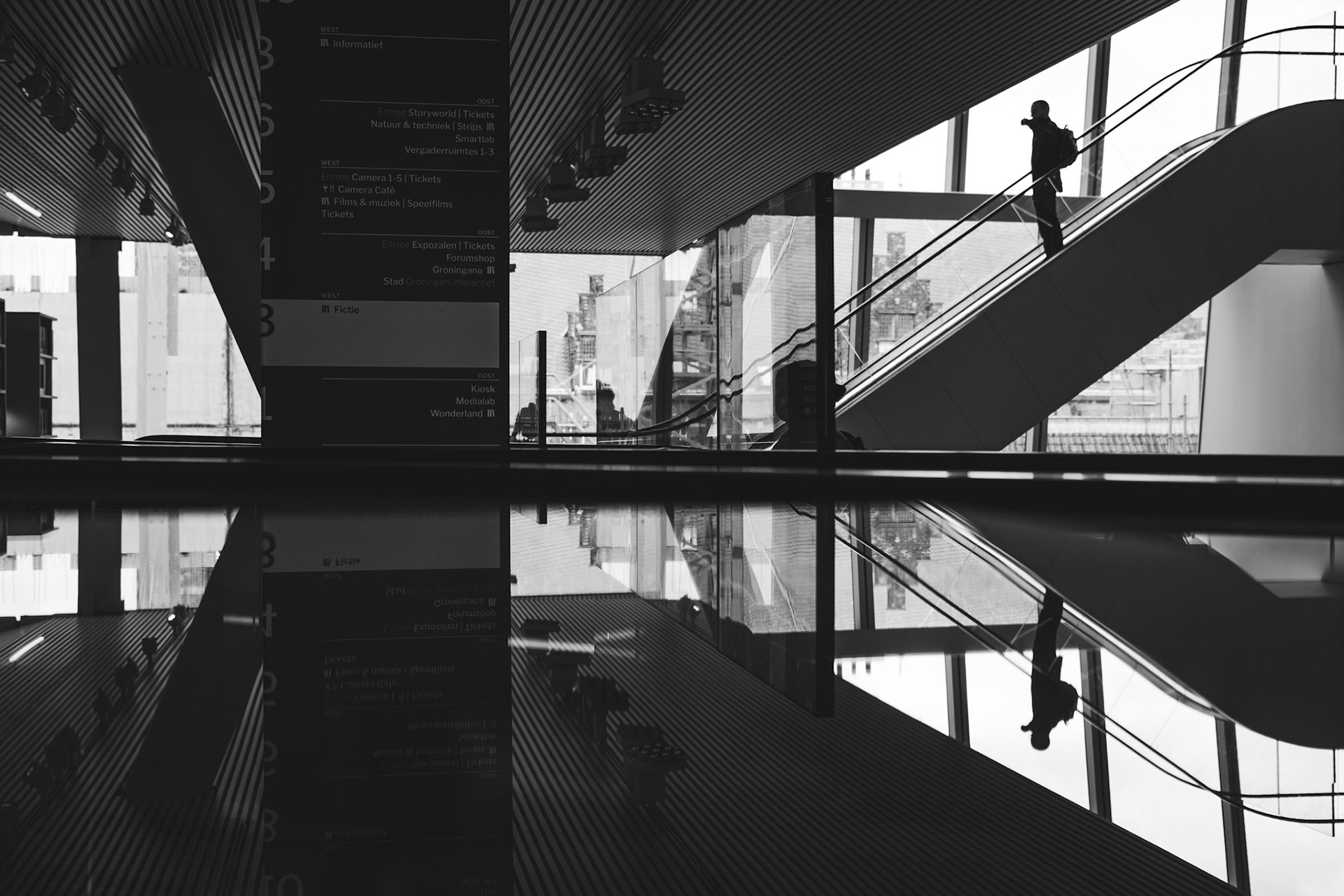 Zwart-wit spiegelwereld: reiziger in beton en glas.