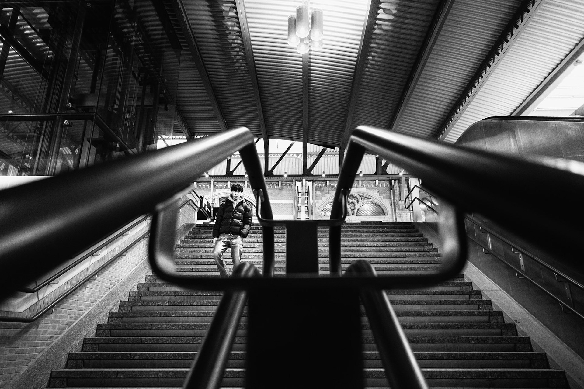 Stationstrappen: subframing via leuningen isoleert silhouet in zwart-wit compositie.