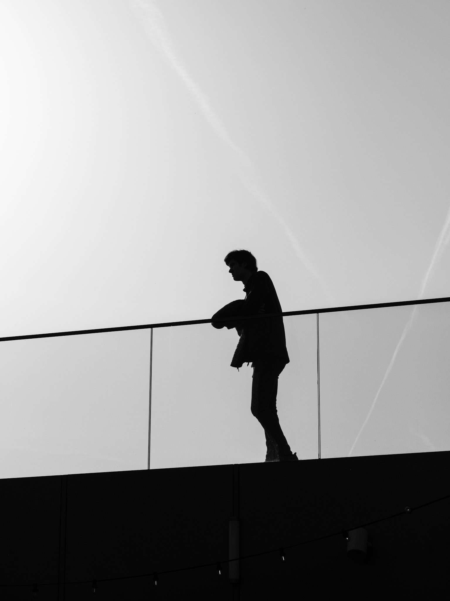 Op het Forum-dak leunt een eenzame figuur over de reling, verloren in gedachten tegen oneindige leegte.