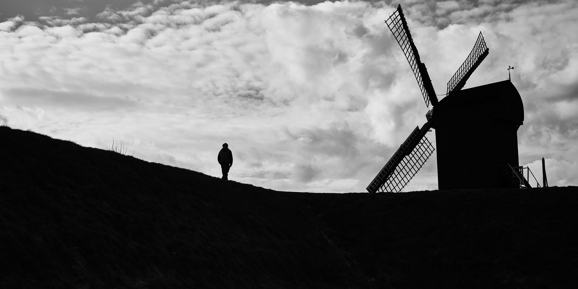 Eenzame figuur voor de molen, dynamisch gebalanceerd tussen grond en hemel.