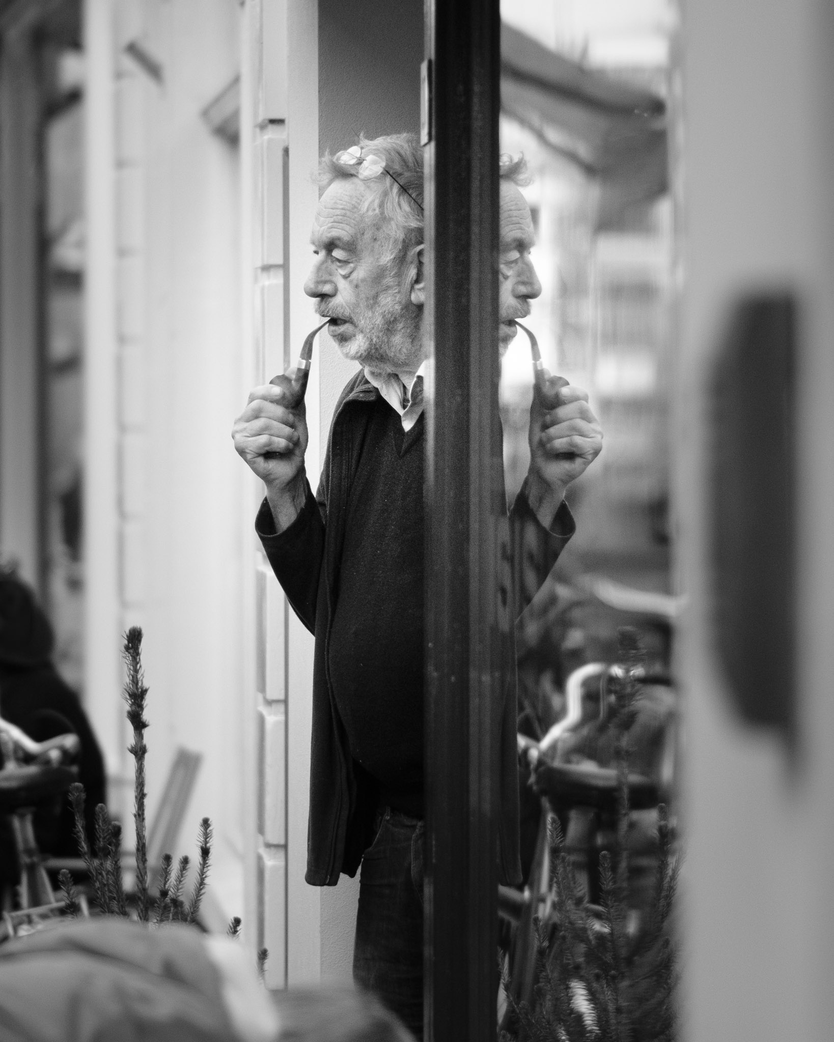 Hij steekt de pijp op in zijn spiegelbeeld, tussen fietsen en takken.