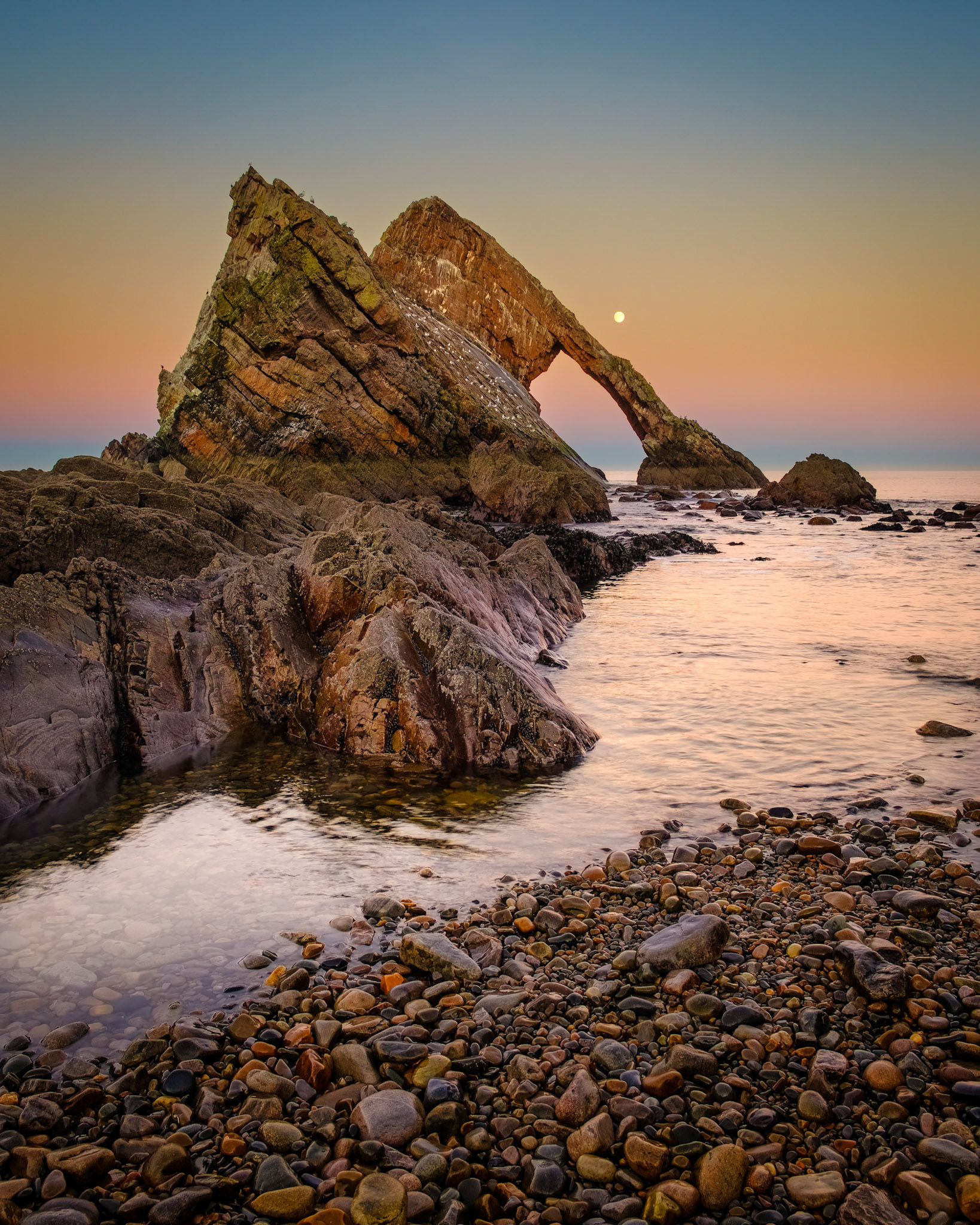The full moon rises over Bow Fiddle Rock at Portknockie, north east Scotland