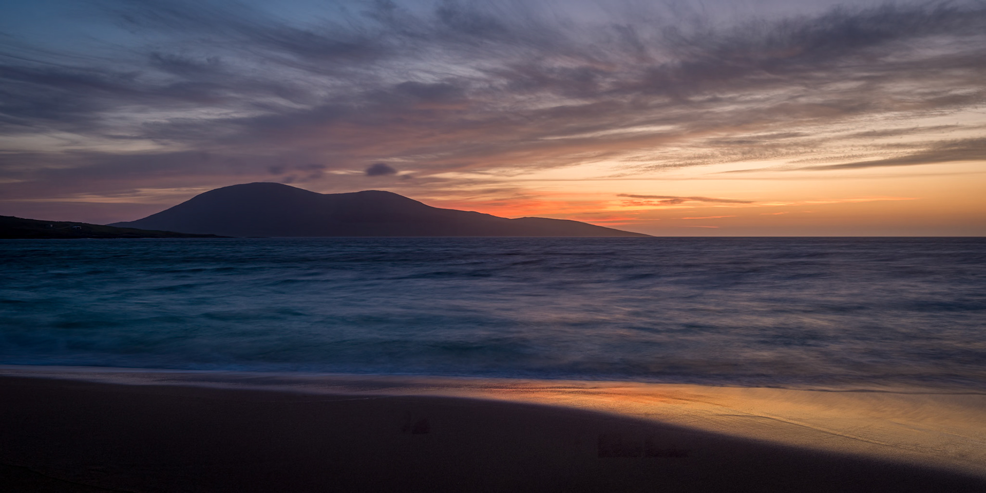 The sunset sky reflected in wet sand at Traigh Mor, Isle of Harris, with Toe Head on the horizon