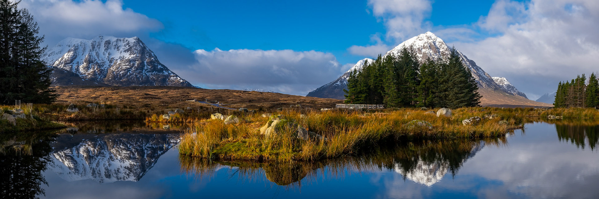 A panoramic view of Meall a'Bhuiridh and Buachaille Etive Mor in Glen Coe, Scotland, reflected in the pond at the Kingshouse Hotel