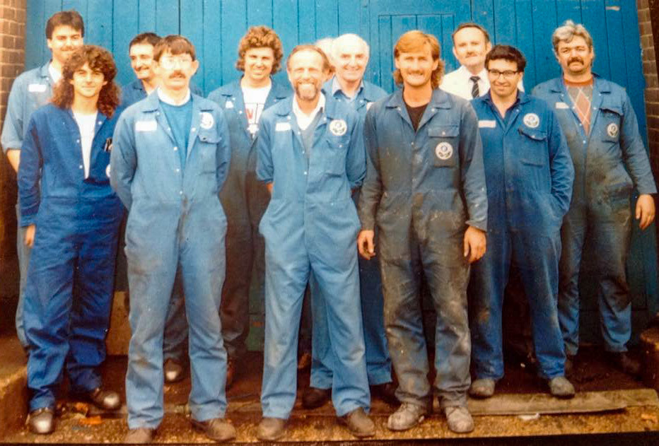 1980's Exeter. Gillian Chambers recognises Andy Callaghan, Mike Knight, John Boucher?, Don Holding, Chris Sercombe, Bill Tapp. Liza Fairclough adds "Marcus was at the front on the left hand side with long curly hair, Andy stood behind him". Helen Gregory and Marie Sluman identify Ron Fairclough, middle front with beard, and add that our dad Ron Yates was boss of the garage at one time and our brother Steve Yates worked in the garage also." Jimmy Reid adds "Marcus Saunders (front, left hand side with long curly hair) remained in the garage spraying lorries but Roy Edwardson (far right at the back), went on to drive. They nicknamed him “Badger” in Thornbury when he used to come to uplift milk for Exeter after the closure."(Courtesy Phillip Budd)