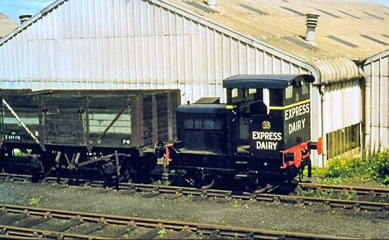 1962 Ruston &amp; Hornsby 0-4-0 diesel locomotive at the Express Dairy bottling plant, Morden South. Mike Morant comments "The picture was taken from the window of a passing EMU whilst travelling towards Sutton from Wimbledon in September 1962." Peter Roper comments "Driving it, and its successor, was fun-I did it several times. You had to anticipate the (lack of) braking, especially when shunting full wagons. The two unloading bays took 14 tanks, 7 each side. But on some nights we might receive up to 18. On one famous occasion, a member of staff let it run off the catch points, partly blocking the Wimbledon line 😮. I had to phone the signaller, urgently!!" (Slide taken by Mike Morant, courtesy Paul Smith)