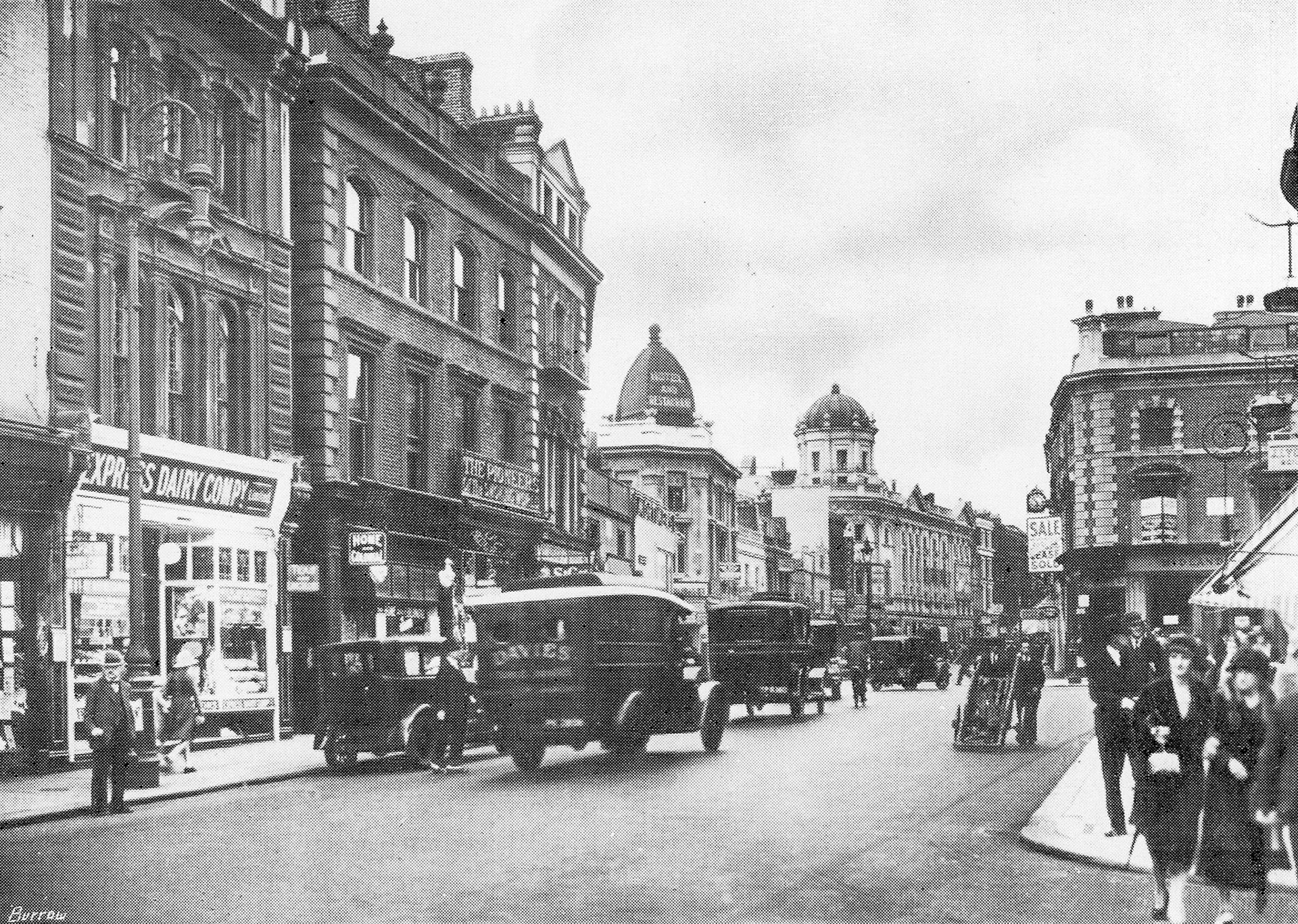 1920s? Notting Hill Gate shop. Tim Bannerman comments "Only the Coronet cinema in the distance remains, the rest cleared for road widening in the 1960s.". The Express shop at 113 Notting Hill Gate (in 2025 'Frame Set &amp; Match picture framers) was next door to the Coronet (now a theatre and dance school) so this is another shop in the same street, near the current tube station and Pembridge Gardens. (Image courtesy Paul Luke)