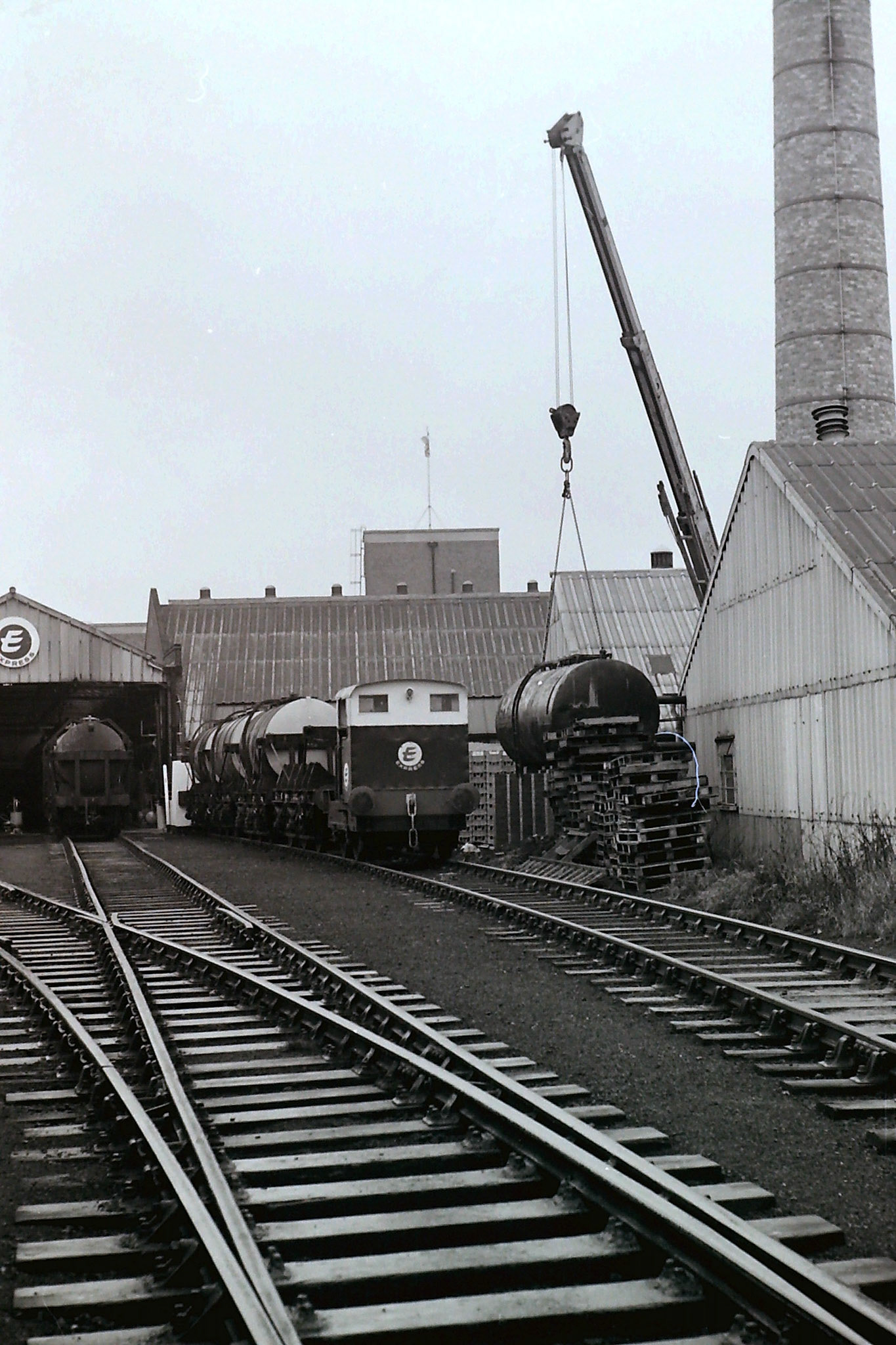 1970's South Morden rail unloading bay with water tank being repurposed. Raffaele Ralph Phillips comments "I started my apprenticeship in 1970 in the building far right, as a Motor Vehicle electrician. The tank being positioned was used to condense steam that when cooled became distilled water used for topping up lead acid batteries. It supplied our garage and the EVM depots who maintained the milk floats and forklifts." (Photographer Sam Jones)