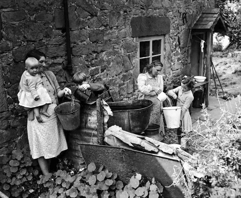 1956 Collecting water at Ruyton X1 Towns. Caroline King comments "I believe this is my godmother Alice Bradbury who lived in Ruyton with her husband Jack and children Maureen and Malcolm. I don't don’t know where the cottage in the photo is but they later lived in Bridge Cottage." Martin Price adds "My grandparents lived in Ruyton XI Towns, until the late 50's there was no mains water. Rainwater was collected for cleaning, washing and baths, washing of clothes (dolly and roller mangle, then everything dried hanging from lines stretched over veg plots). The dairy delivered churns of potable water as the use of water in cheesemaking had lowered the aquifers and emptied the wells. Eventually water mains were laid by the Water Board. Grandfather lived IN Gooseberry Lane by the church, and my cousins lived firstly in Cliffe and then Fiveways, they are all Jennings's. There was no electricity, so paraffin lamps and radios with rechargeable batteries. Cooking was done over a solid iron range/ baking oven/ fire-side hot water boiler. No central heating but cottage was warm in winter and cool in summer, walls three feet thick sandstone. Just 70 years ago." (Courtesy Lin Keska)