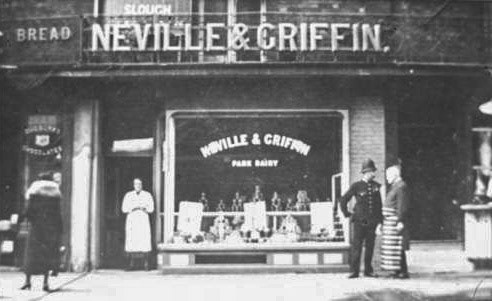 1928 Neville and Griffin Grocers at 84 High Street, Slough."The window of Neville and Griffin also advertises Park Dairy who may have supplied them with local dairy products. Neville and Griffin occupied the shop from 1903 until 1978. The shop to the right appears to be a butcher's and the man talking to the policeman is probably the butcher in his striped apron. The shop on the left is advertising Cadburys Chocolate." (Courtesy Reg Harrison Collection, Slough Library)