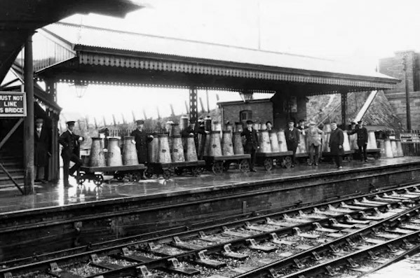 1928 Highbridge Station, Somerset. Milk churns sit on platform barrows having just been dropped off by the dairies. They await an incoming train to pick them up. Highbridge station opened in June 1841 and is now known as Highbridge and Burnham. (Courtesy STEAM - Museum of the Great Western Railway)