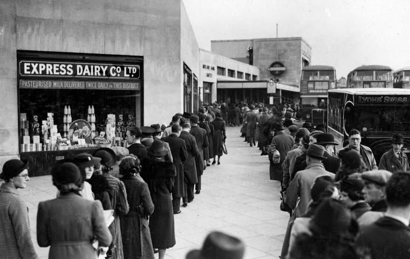 1938, March. Morden Underground station; a queue of passengers waiting for workmen's tickets with Express Dairy shop advertising " Pasteurised Milk Twice Daily in This District". (Courtesy London Transport Collection)