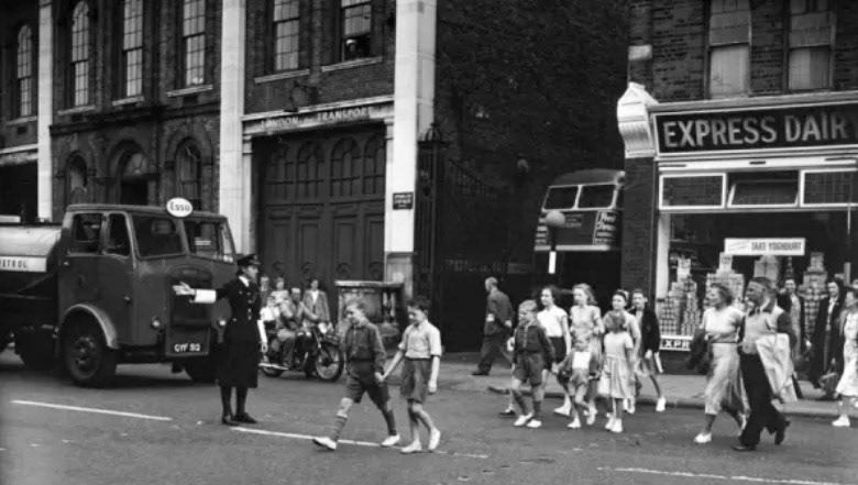 1951 Express shop with woman police officer (Jessica Penfold or Leach) on traffic duty in London, helping adults and children cross the road safely. (Courtesy Mary Evans Picture Library)